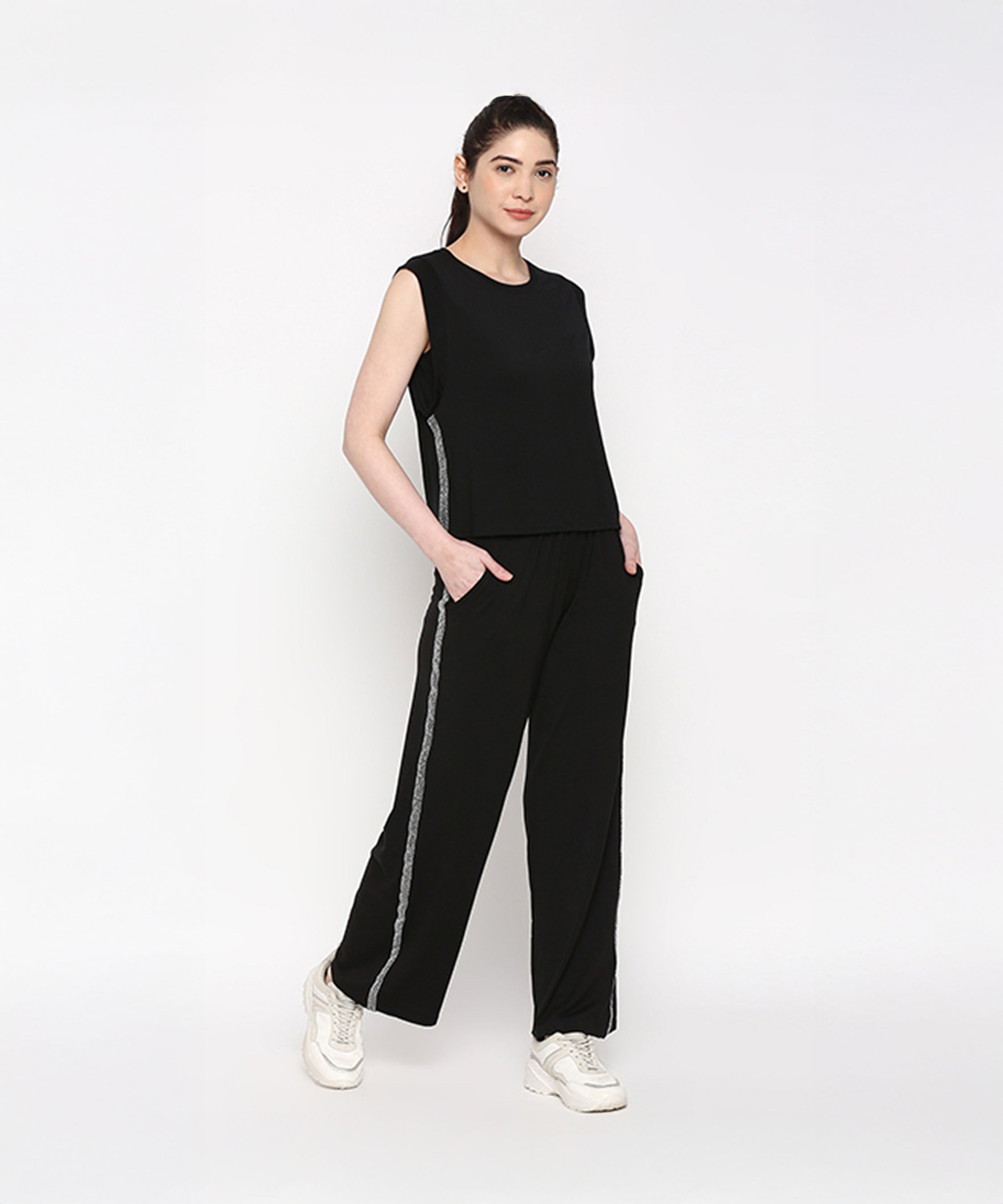 Woman wearing the Comfy Black Set with Side Sparkle—sleeveless top and loose fit track pants with side stripes—posing with hands in pockets.