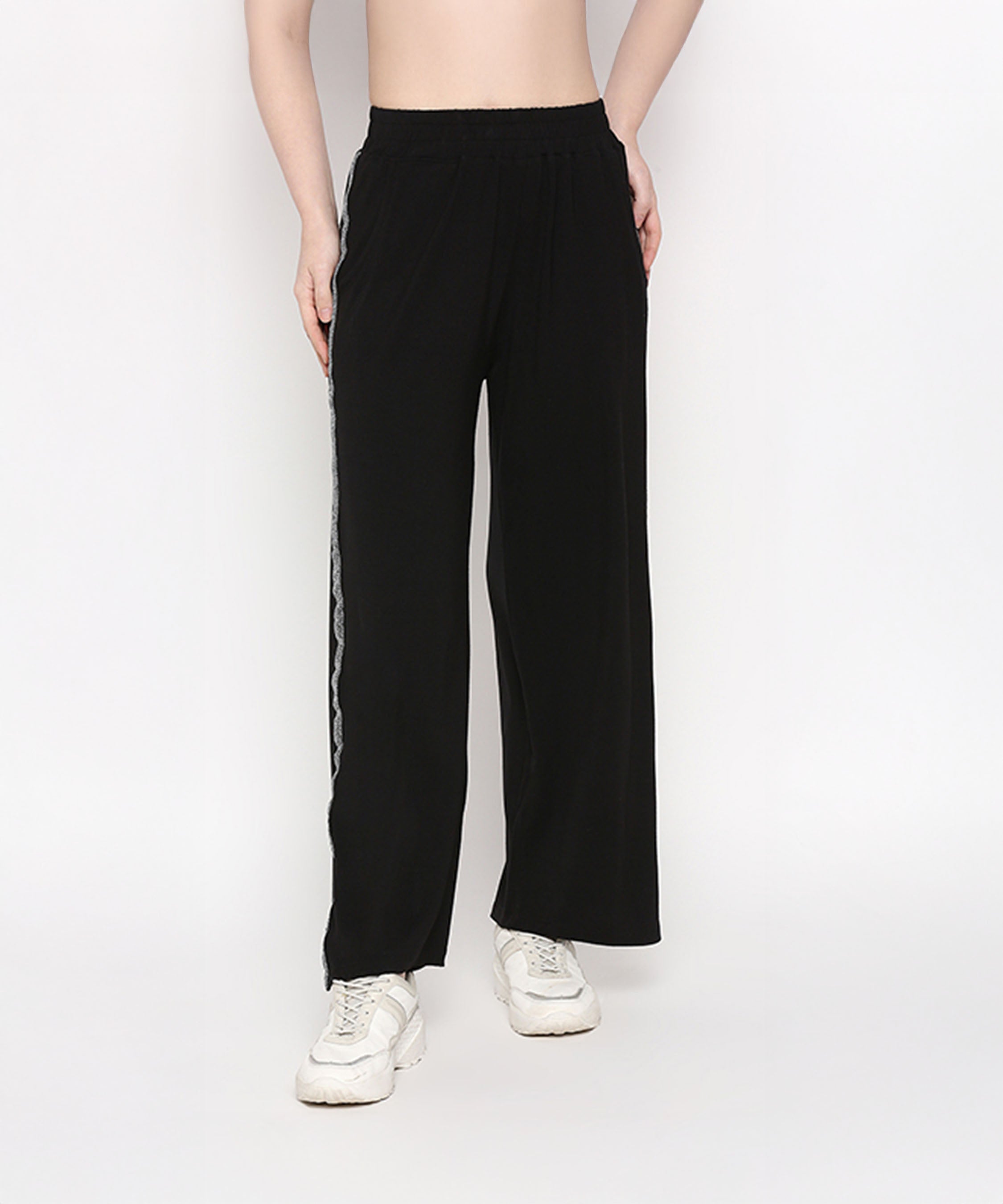 A person wears the Comfy Black Set with Side Sparkle—black loose-fit pants with white side stripes—styled with white sneakers, standing against a white background.