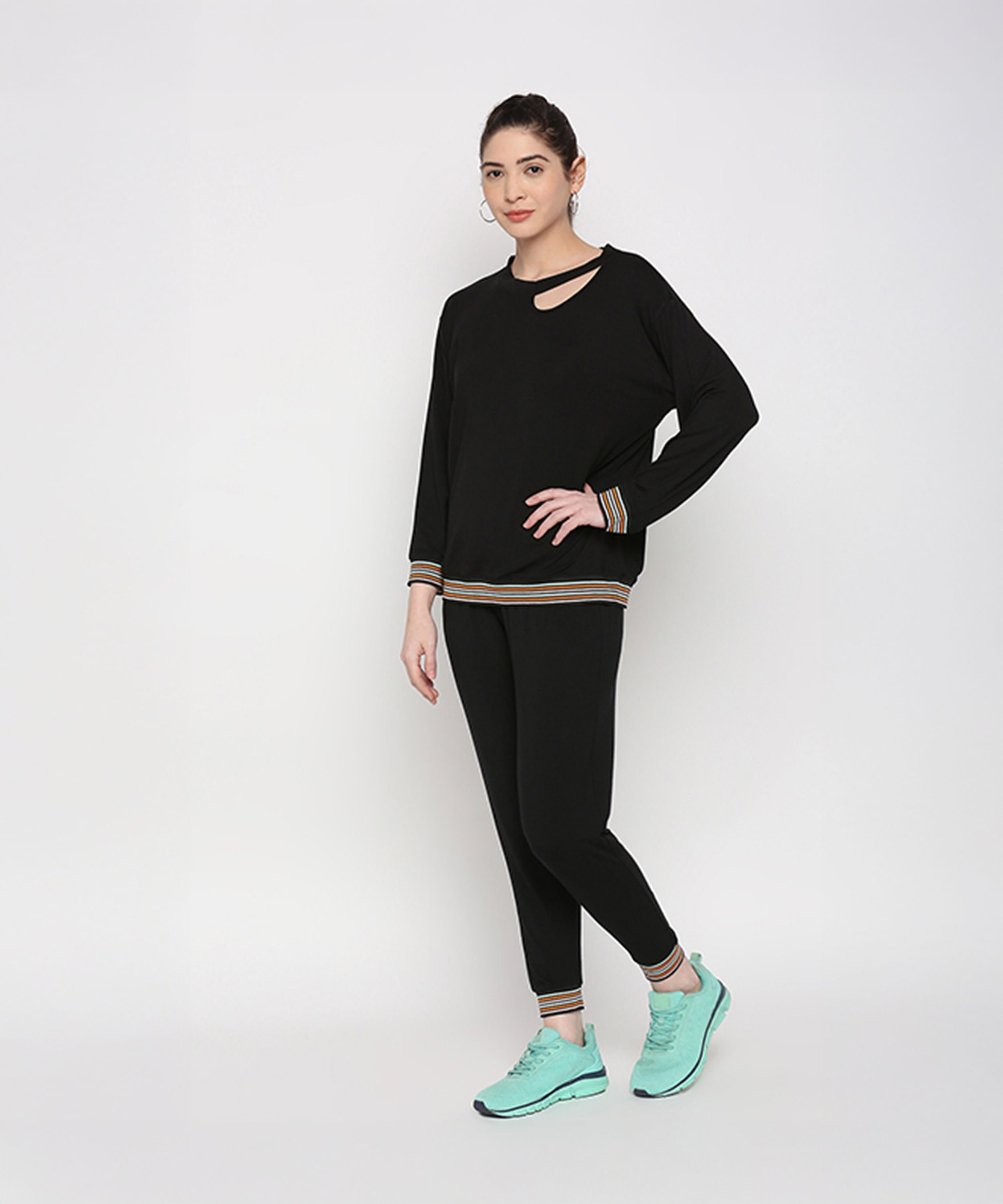 Model showcases the Versatile Black Ensemble—neck cut out top and joggers in soft cotton modal—paired with teal sneakers, against a plain white backdrop.