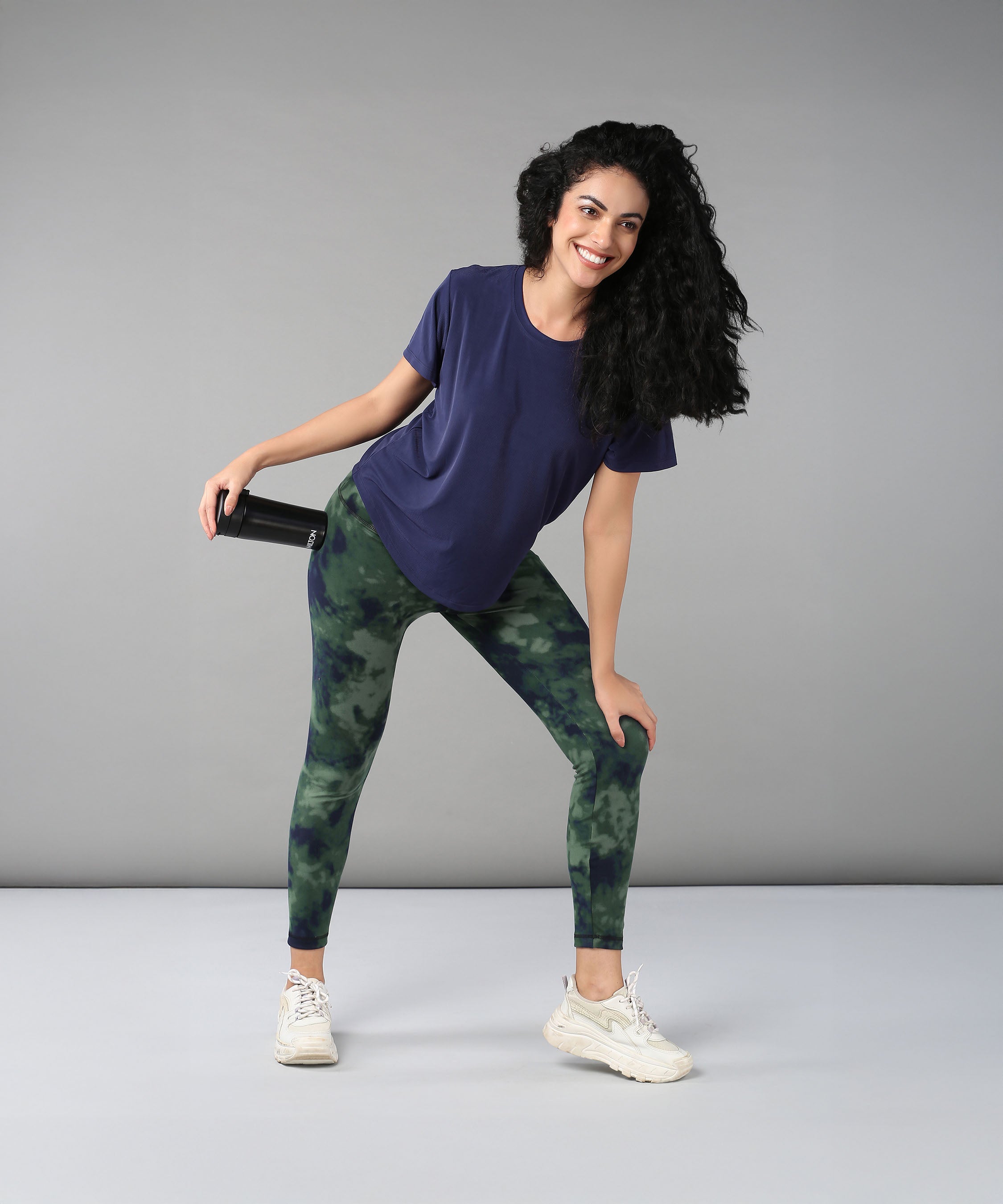 Smiling woman wearing the Functional - Blue Soft T Shirt made from durable, comfortable materials, holding a water bottle and posing against a plain grey background.