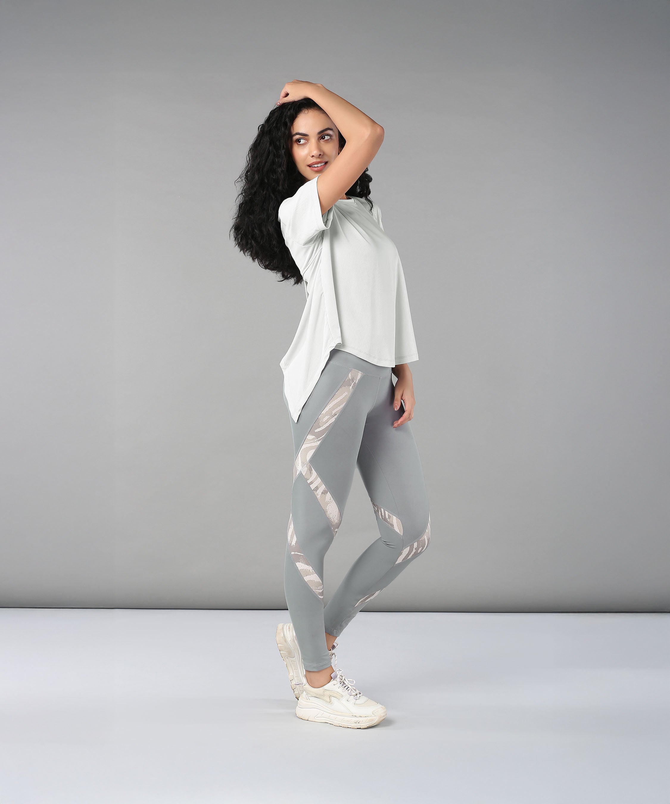 Woman wearing the Grey Top with Patched Legging, made from super soft fabric, poses confidently against a plain grey background.