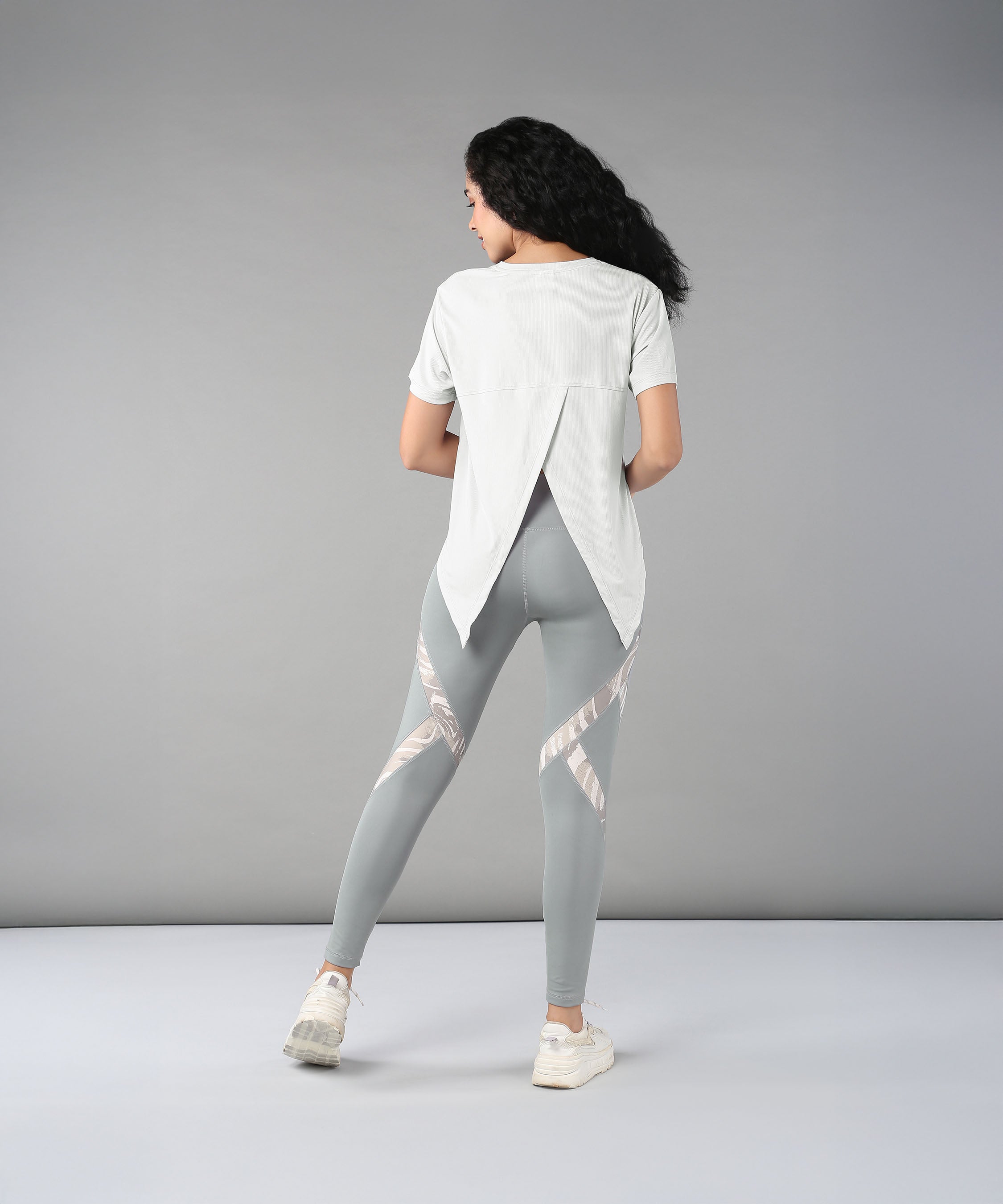 Woman with long curly hair, wearing the Grey Top with Patched Legging made from super soft fabric, stands facing away in a studio.