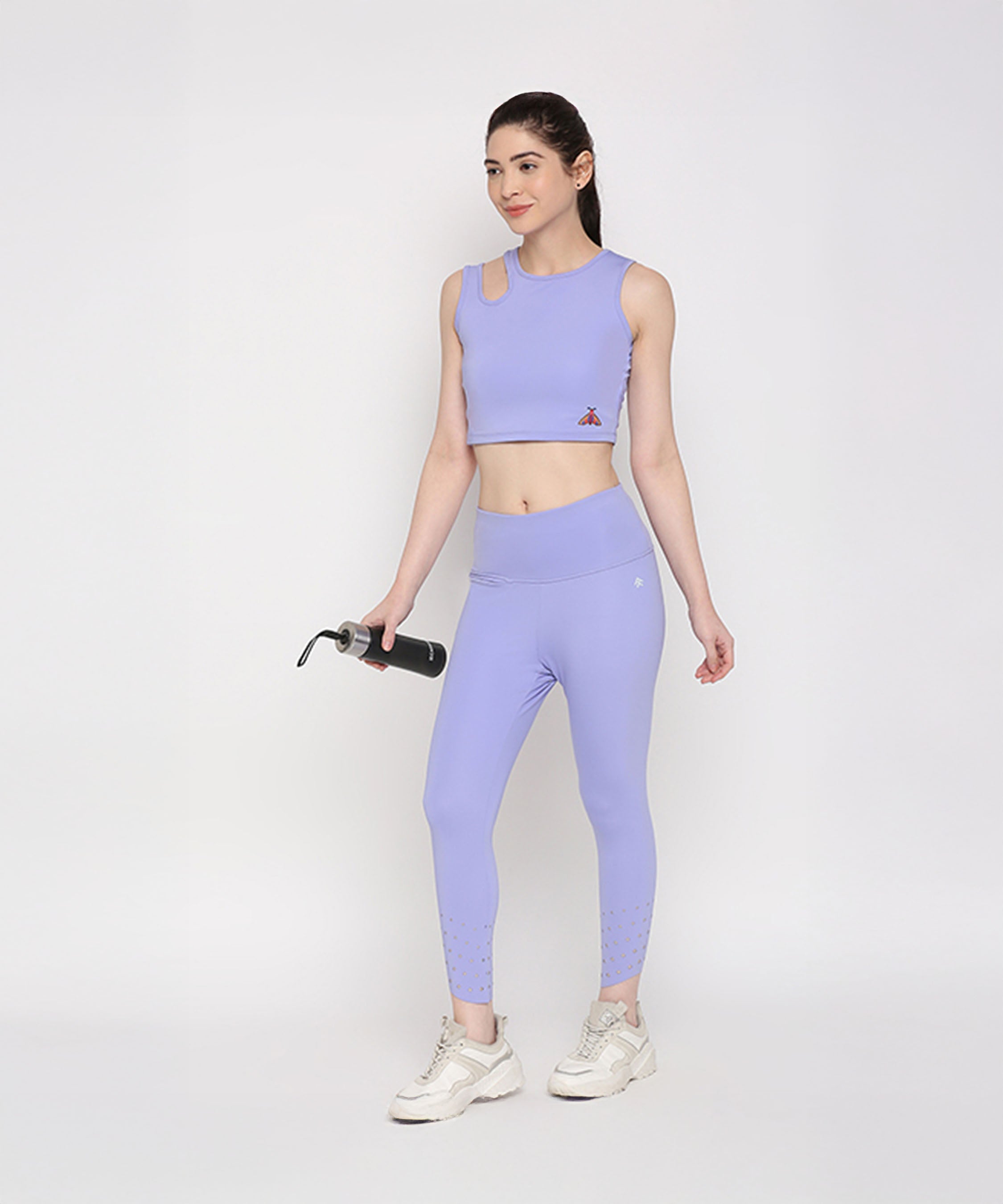 A woman in the Tuna Active Lavender Co-ord Set stands against a plain white background, holding a water bottle—an effortless and stylish choice for women's activewear.