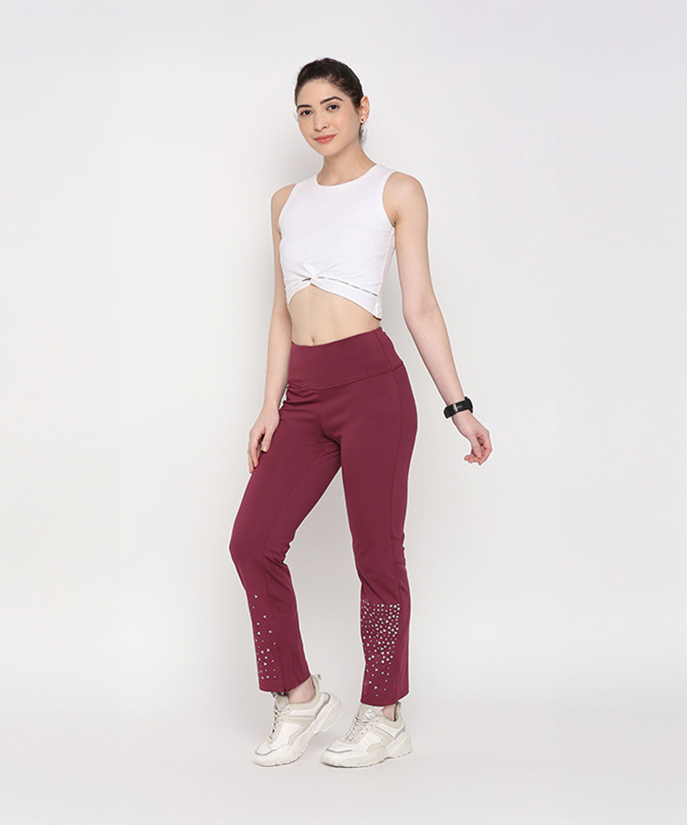 A woman poses against a white background wearing the White Twisted Crop Top and maroon embellished pants.