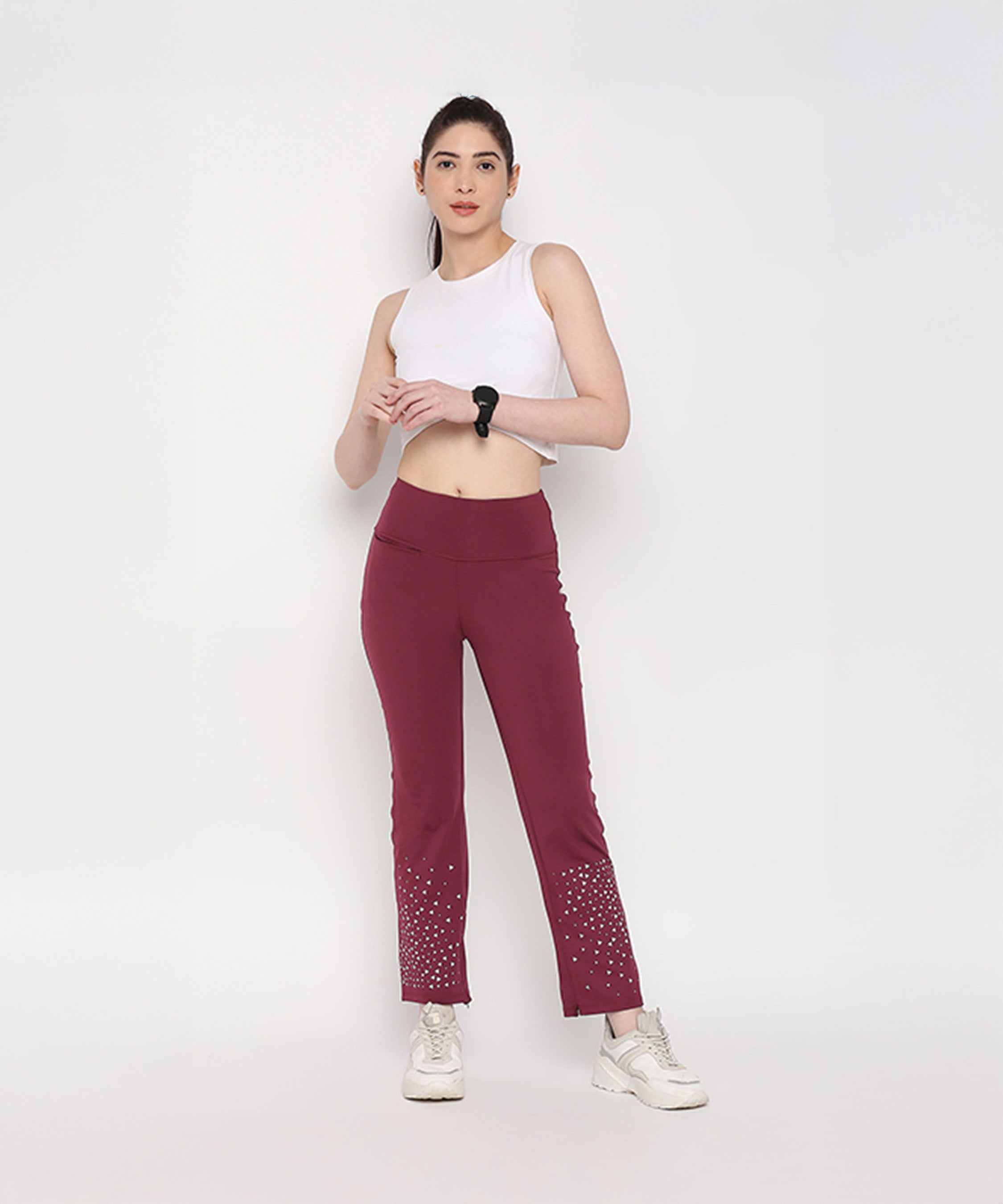 A woman in a White Twisted Crop Top, maroon pants, and white sneakers stands against a plain white background.