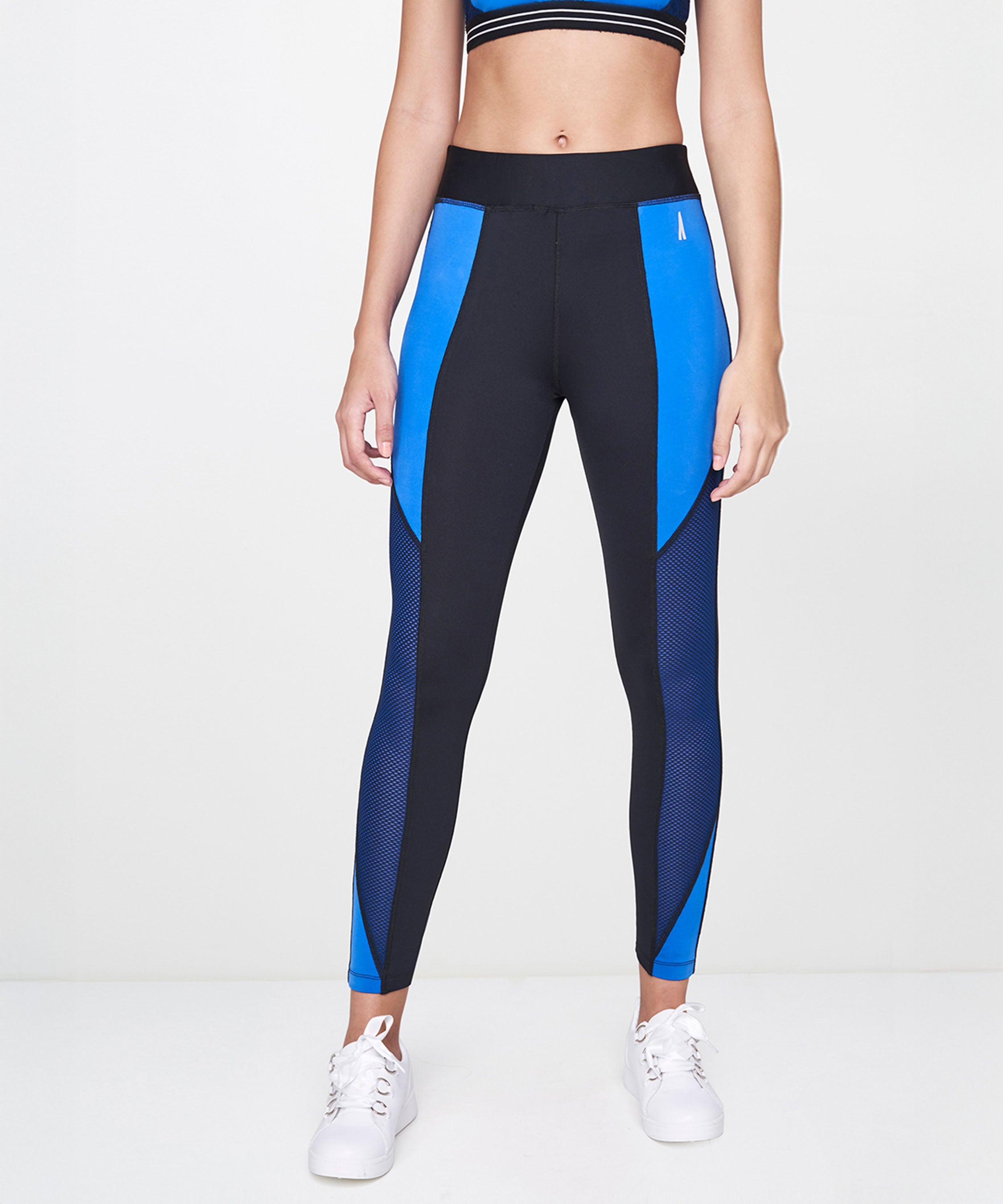 A person wearing Indigo Leggings, a crop top, and white sneakers stands against a white background.