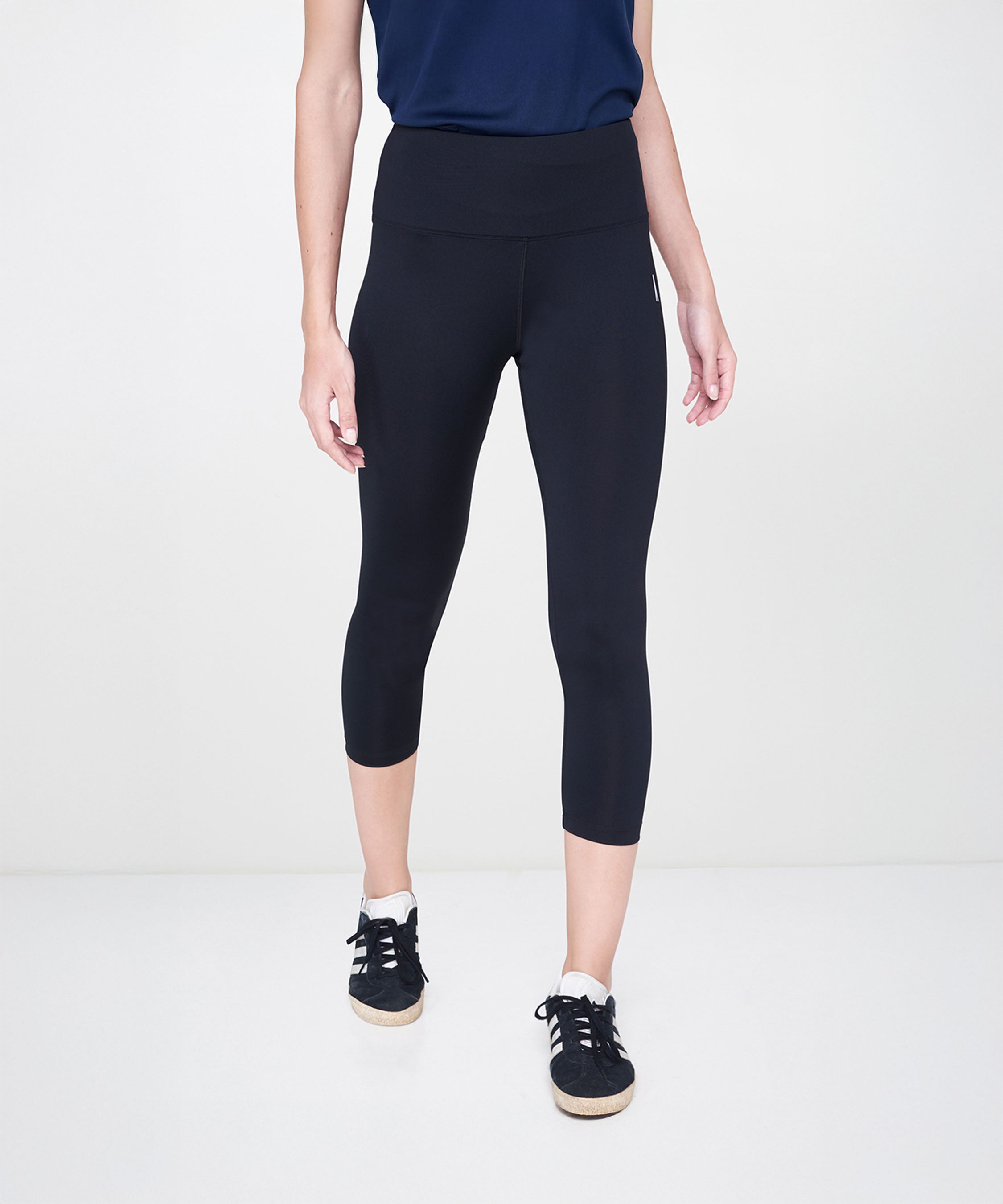 A person wearing Black Leggings with a high-rise waistband, paired with a navy shirt and black sneakers, stands against a white background.