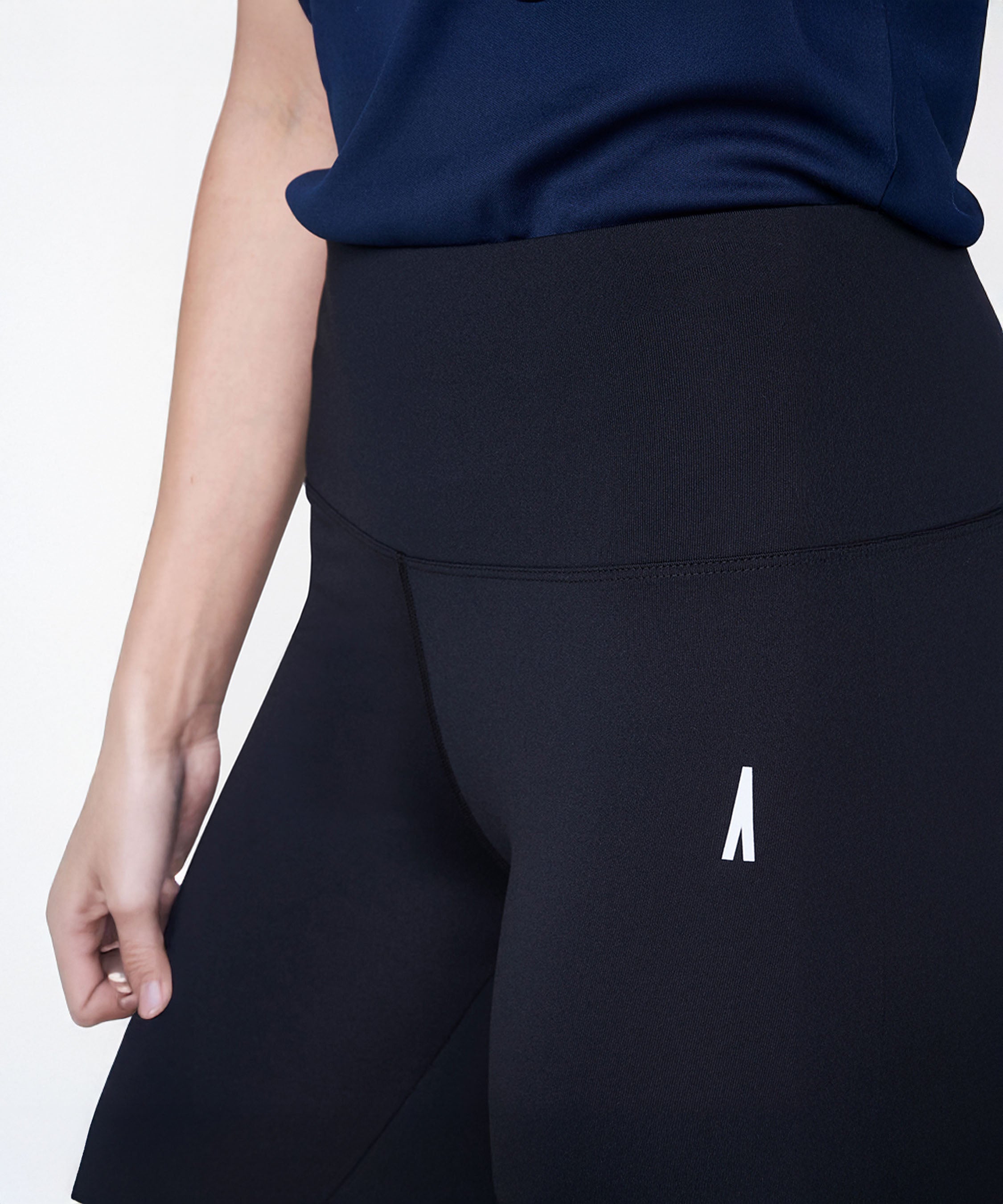 A person is shown wearing Black Leggings with a high-rise waistband and a dark blue shirt, displaying only the lower torso and one arm.