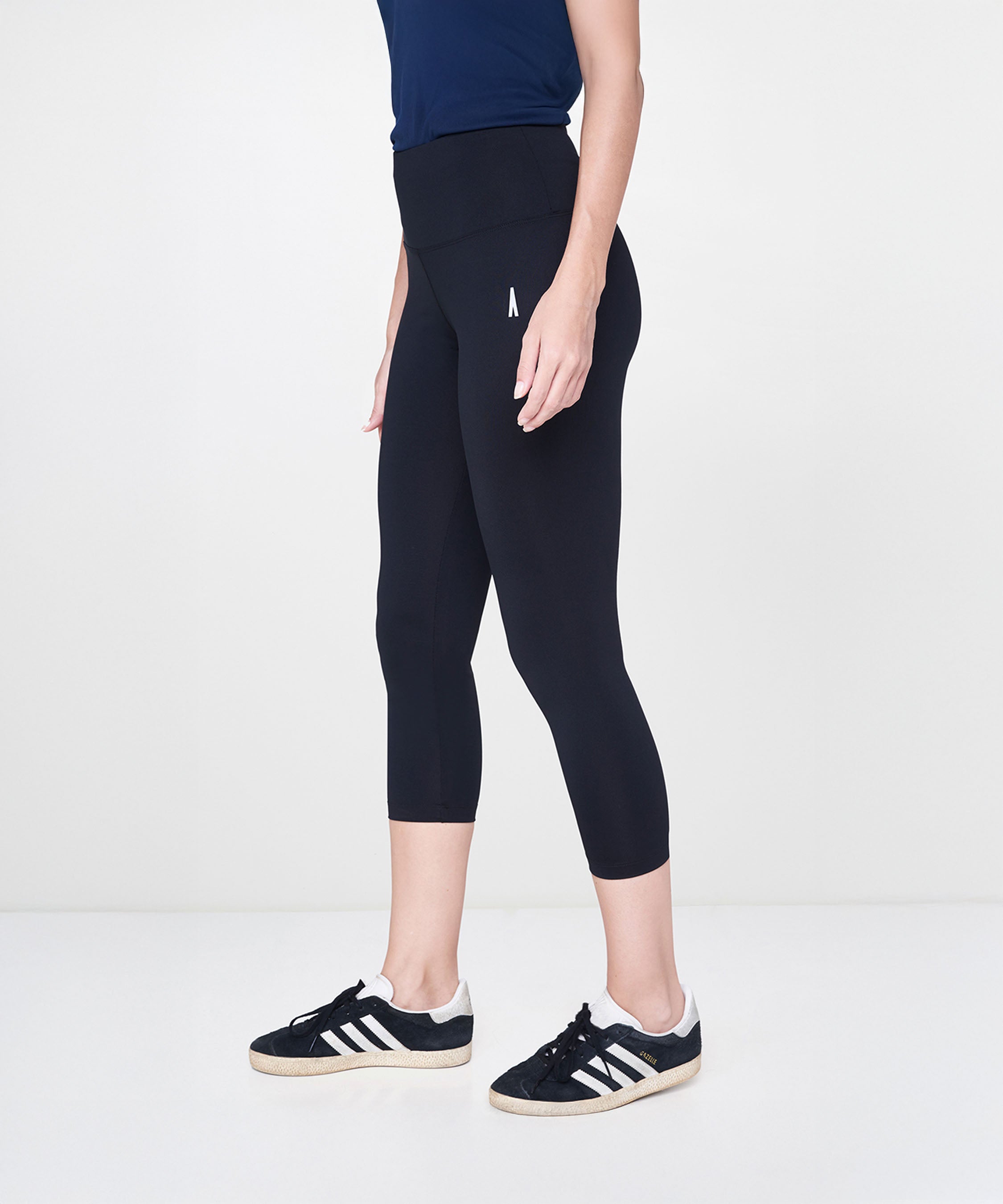 Model in Black Leggings with a high-rise waistband, paired with black sneakers and a navy top, standing against a plain white background.