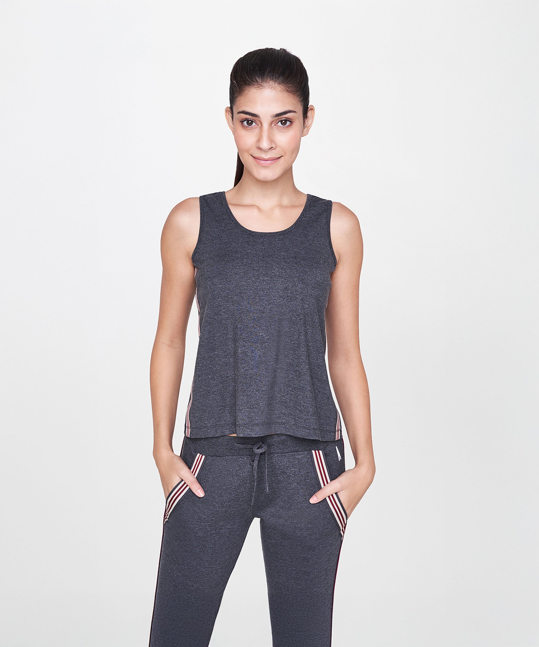 Woman smiles with hands in pockets, wearing a charcoal grey sleeveless tank top and joggers (Grey Sleeveless Tank Top) against a white background. SS19ATHAND34.