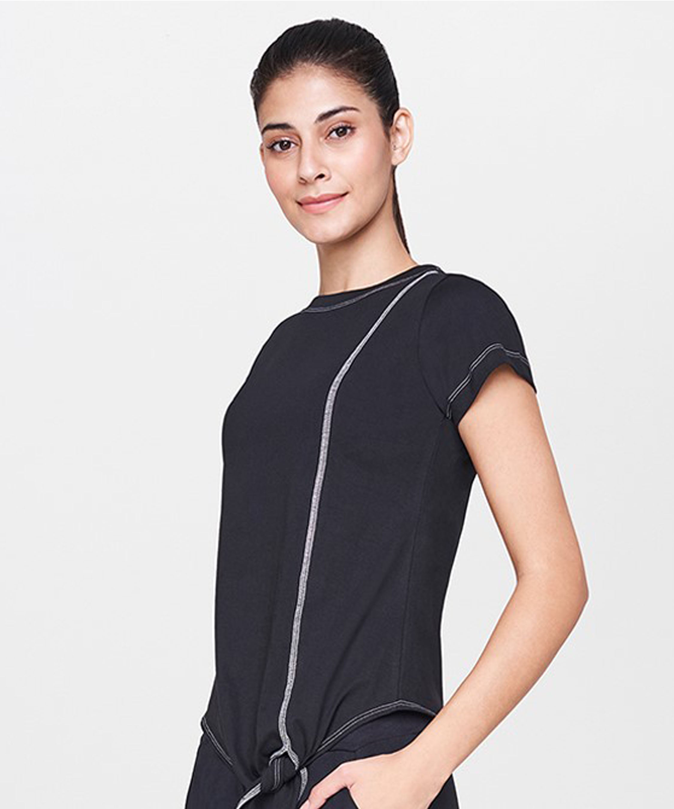 A smiling woman with dark hair in a ponytail wears the Black T-Shirt—a short-sleeved top featuring white stitching, making it an ideal staple for casual outfits.
