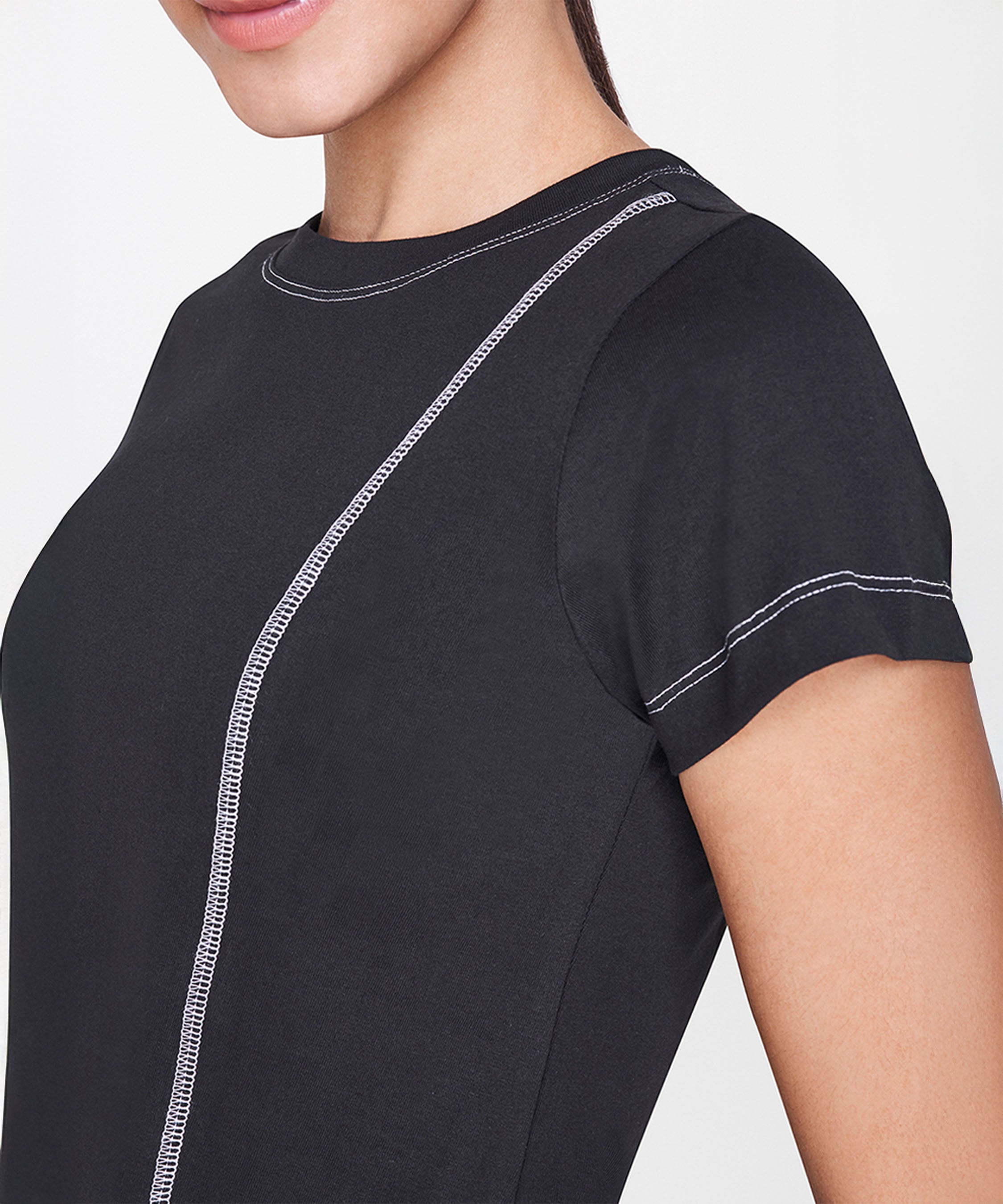 Woman wearing the Black T-Shirt, featuring a fitted cut and white stitching detail, shown from shoulder to mid-torso—a versatile staple for casual outfits.