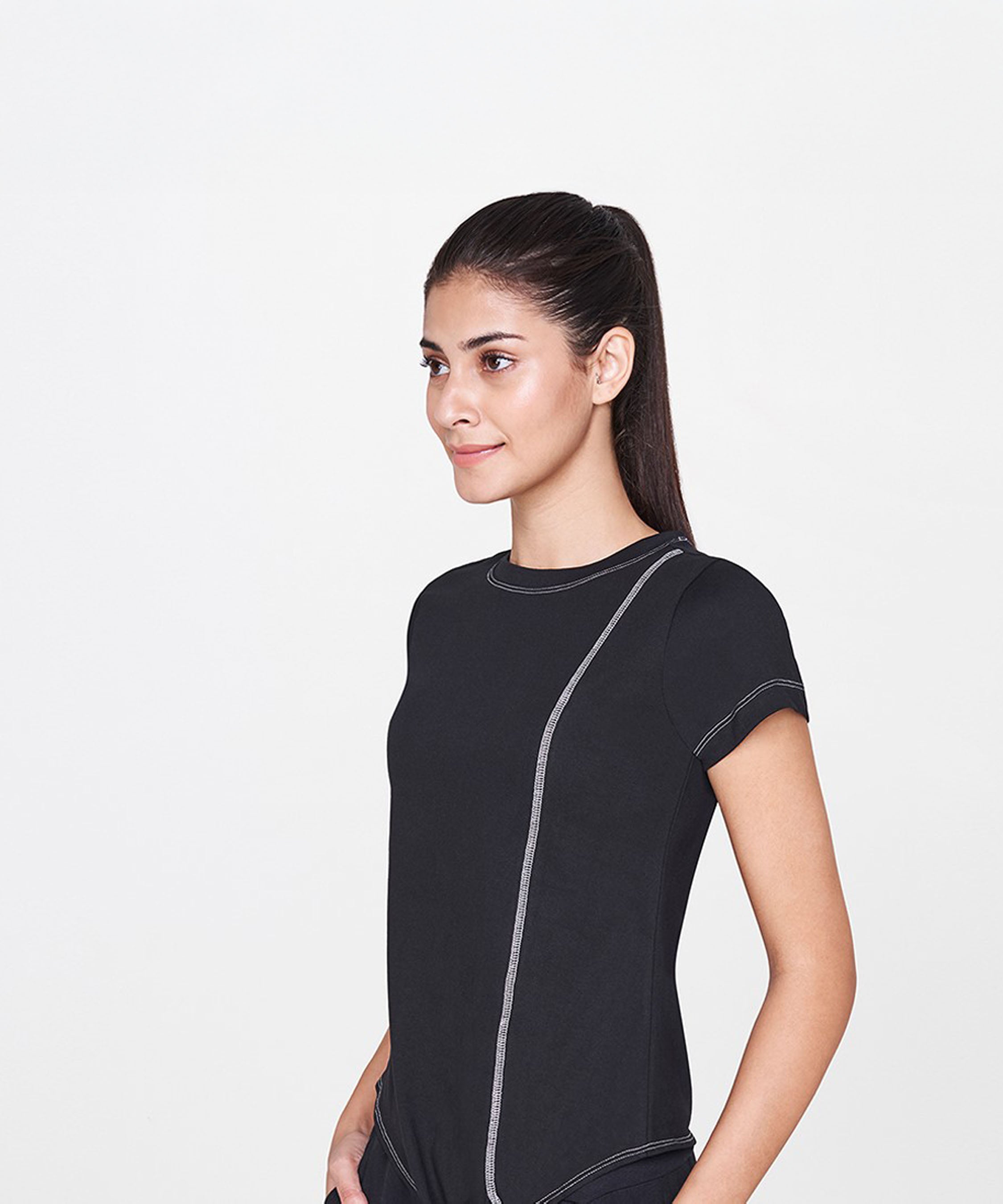 A woman with long dark hair in a ponytail wears the Black T-Shirt, a classic wardrobe staple, while standing against a plain white background.