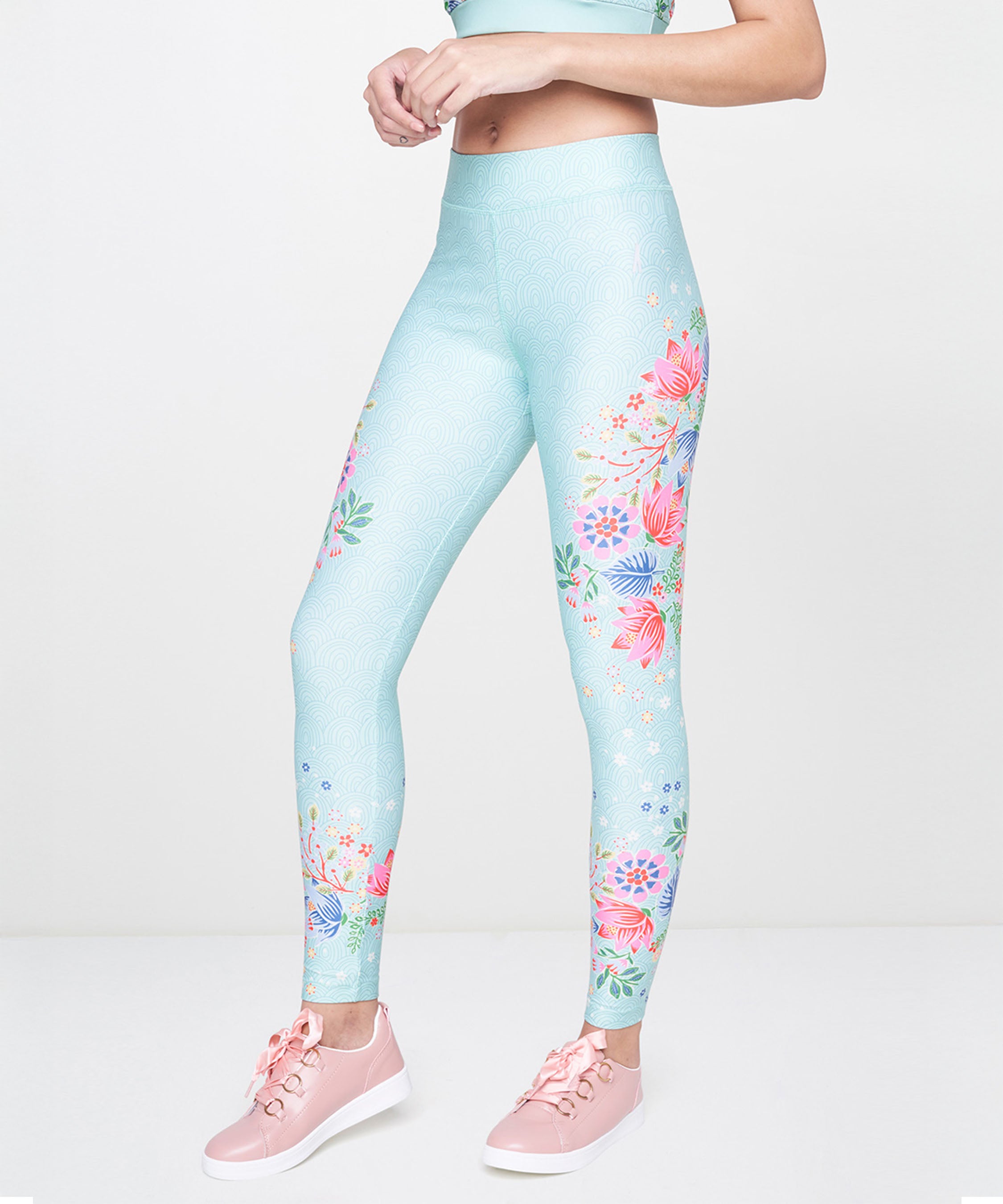 A woman stands against a plain white background wearing Aqua Printed Leggings and pink sneakers.