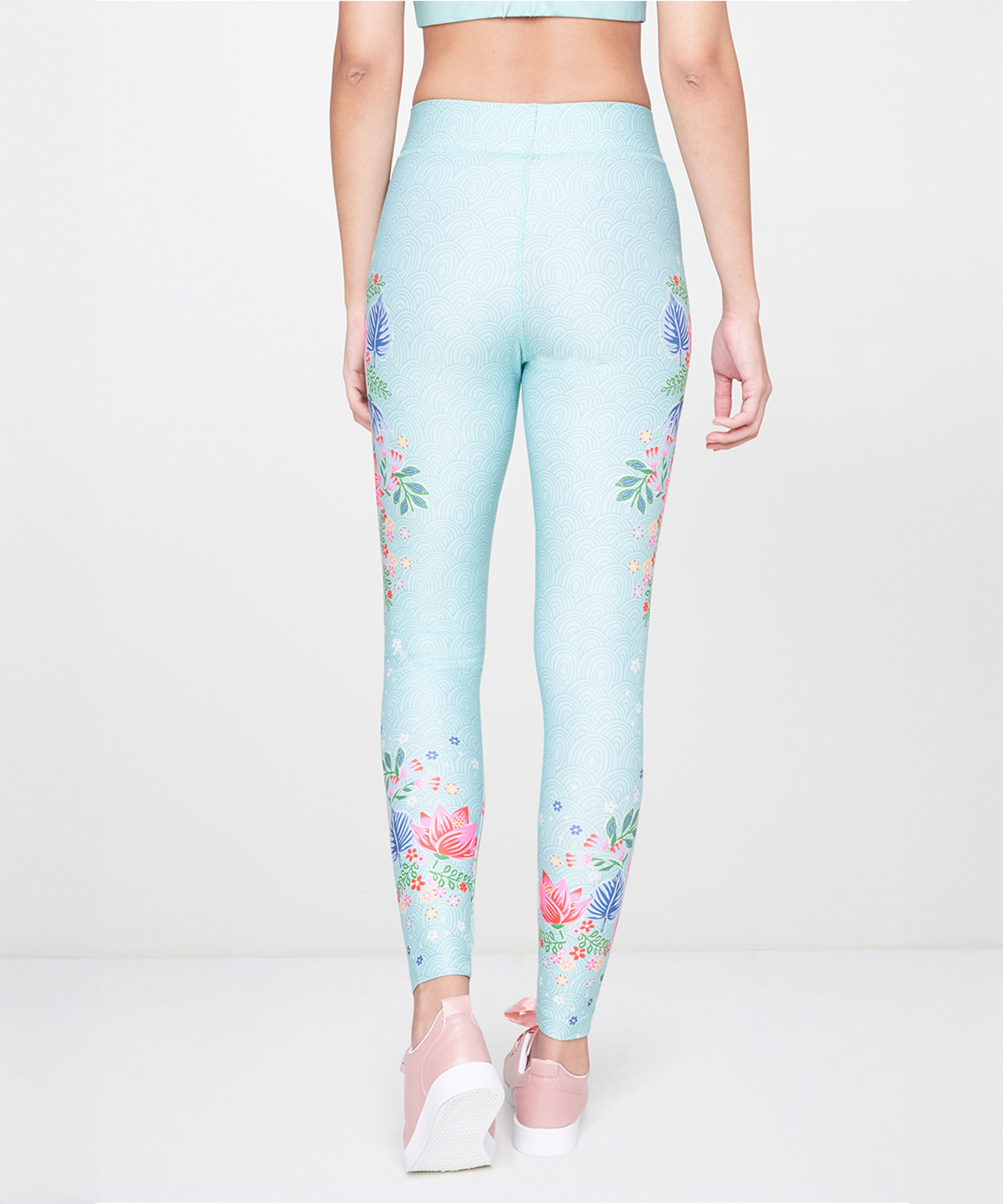 A woman is seen from the back against a plain background, wearing Aqua Printed Leggings and pink shoes.
