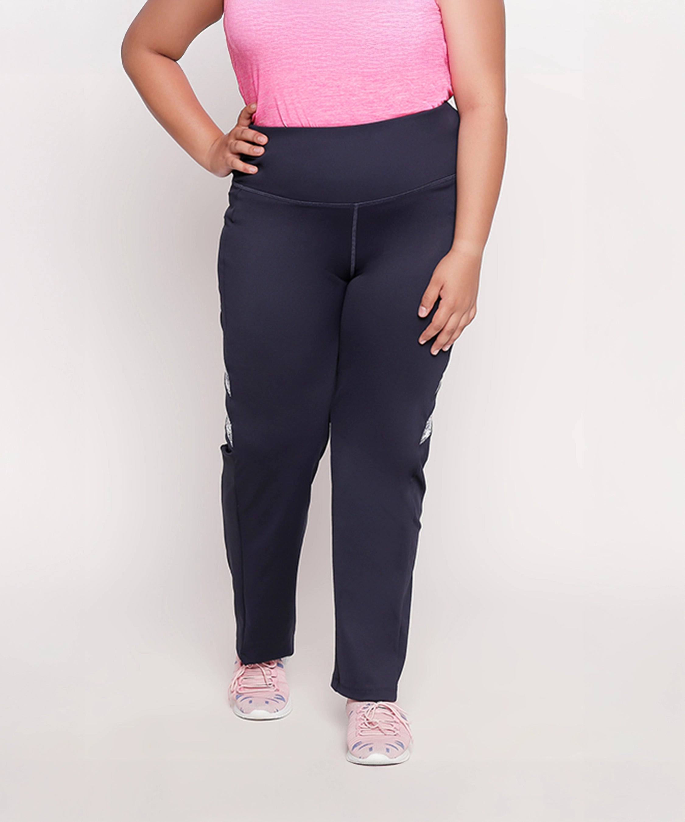 Woman in a pink top, Tuna London Iris Navy Polyblend Track Pant, and pink sneakers, standing with one hand on her hip.