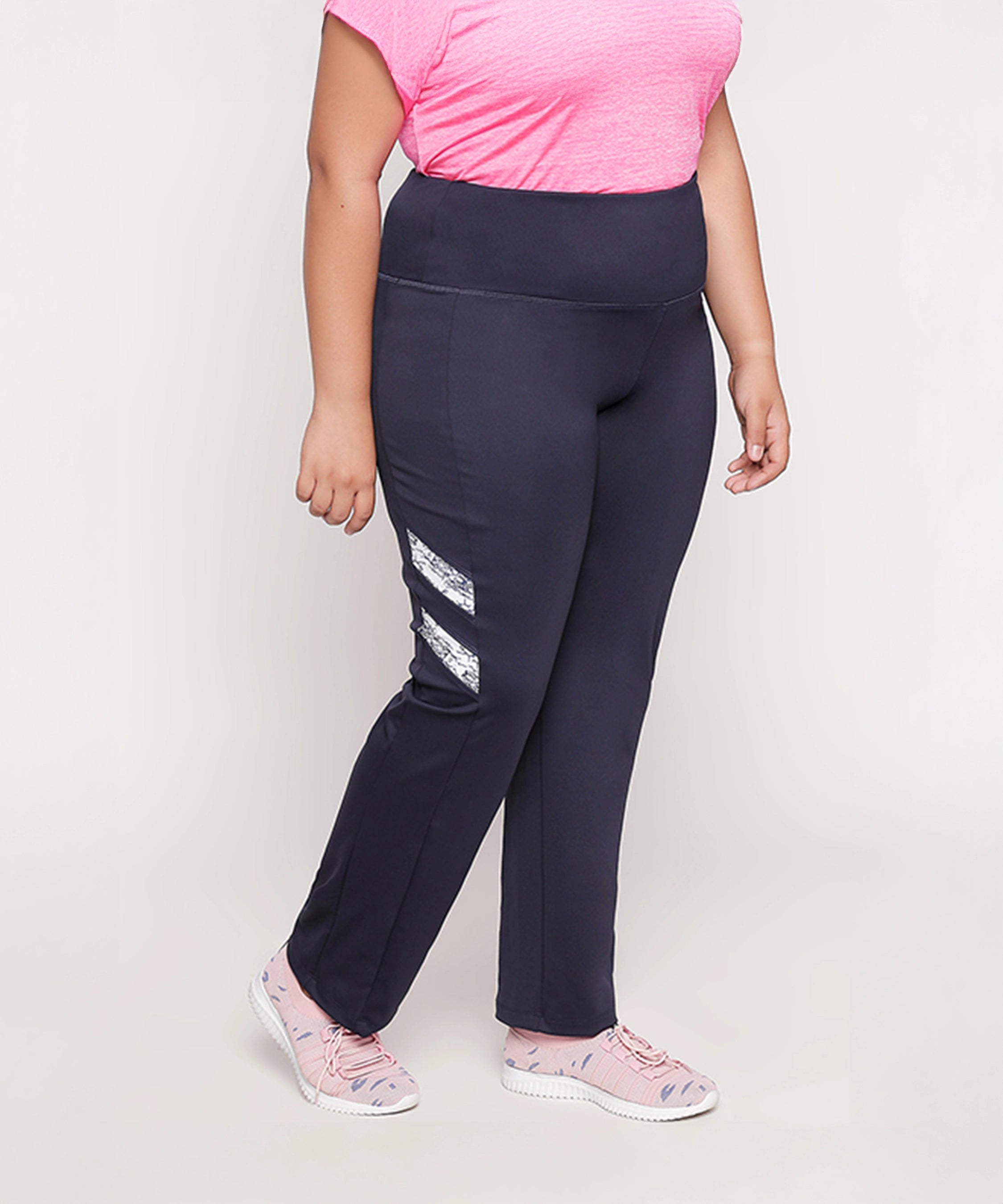 A woman stands against a light background wearing a pink shirt, pink sneakers, and Tuna London Iris Navy Polyblend Track Pant for women.