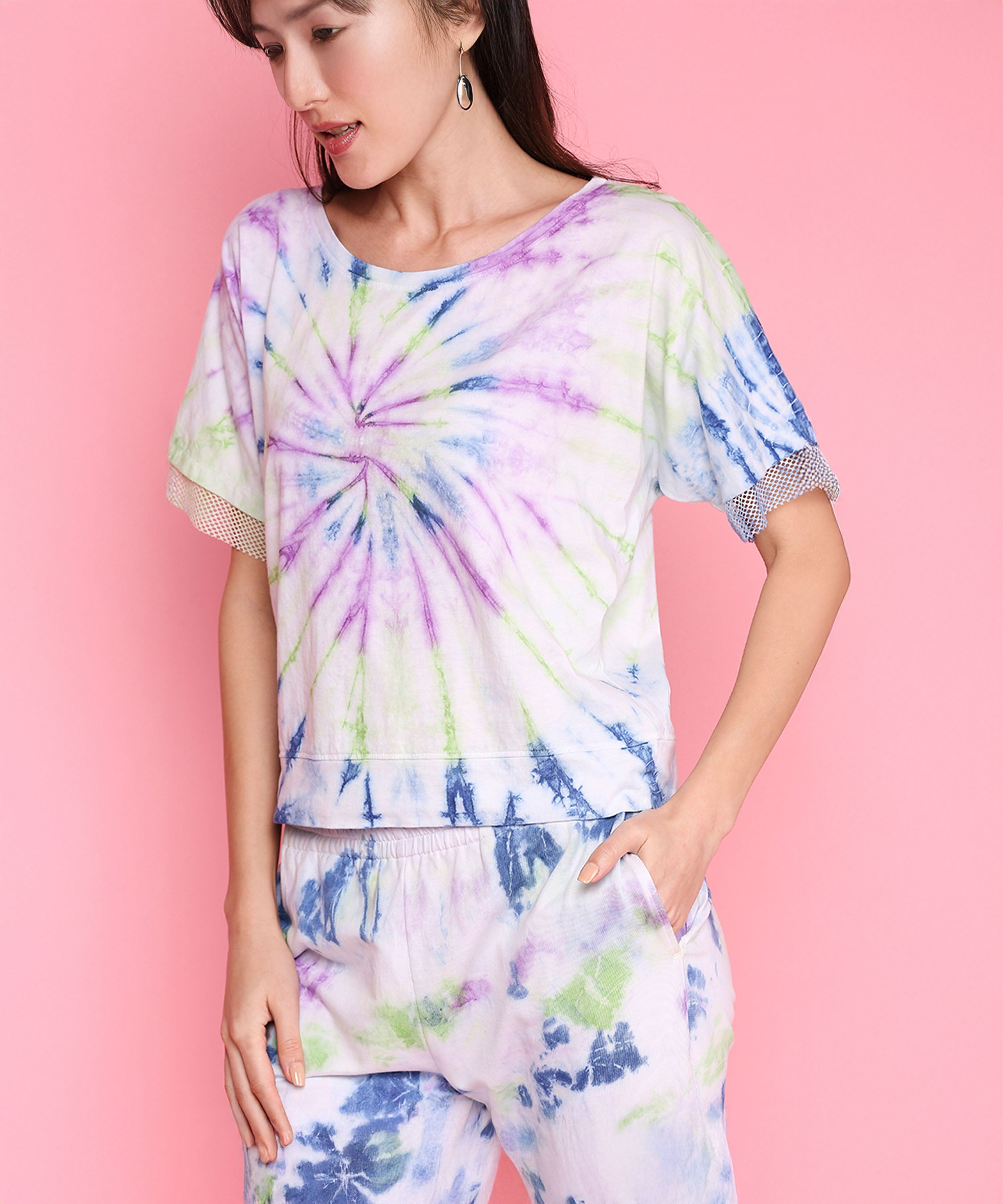 Woman wears the Comfort Fit Tee + Joggers - AW21, made from breathable, hand-dyed fabric. She stands against a pink background, looking down with her hand in the pocket.