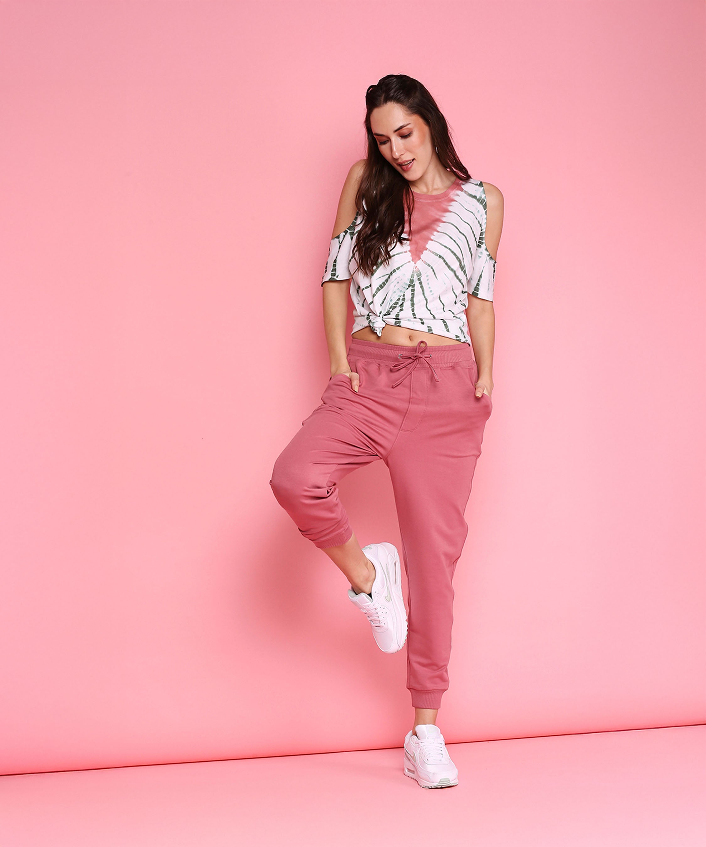 A woman poses in the Cold Shoulder Comfort Fit Top + Joggers - AW21 set, showcasing casual style with playful elegance.