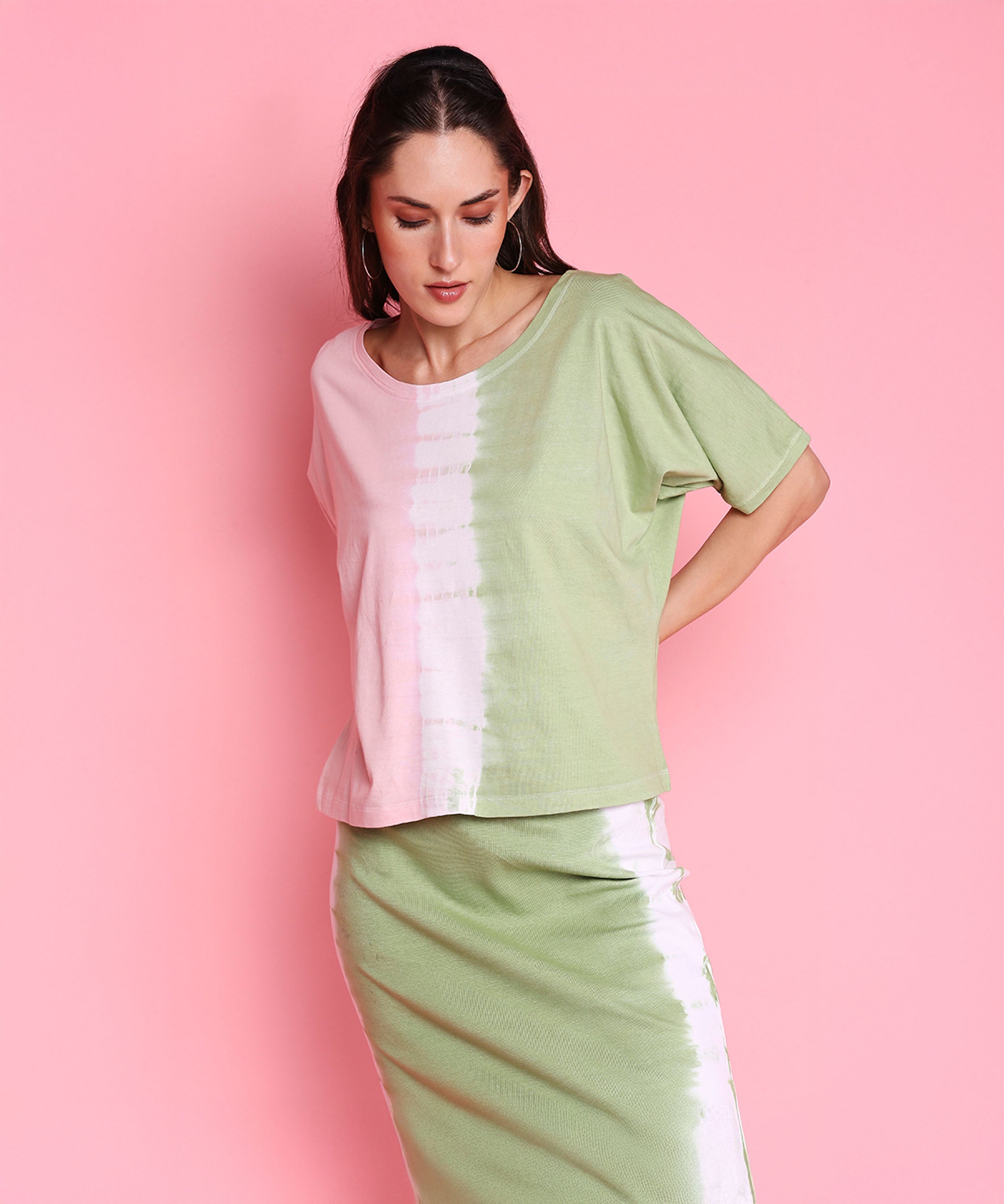 A woman stands against a pink background, showcasing the Comfort Fit Tee and Fitted Tie Dye Skirt - AW21 for a vibrant athleisure look.