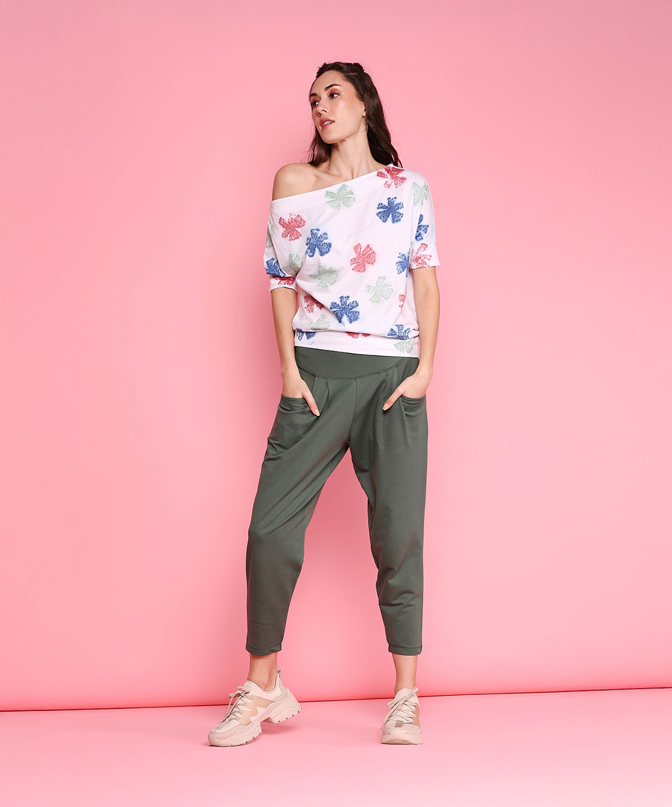 Woman wearing the AW21 One Side Off Shoulder top and Pleated Yoga Pants stands against a pink background.