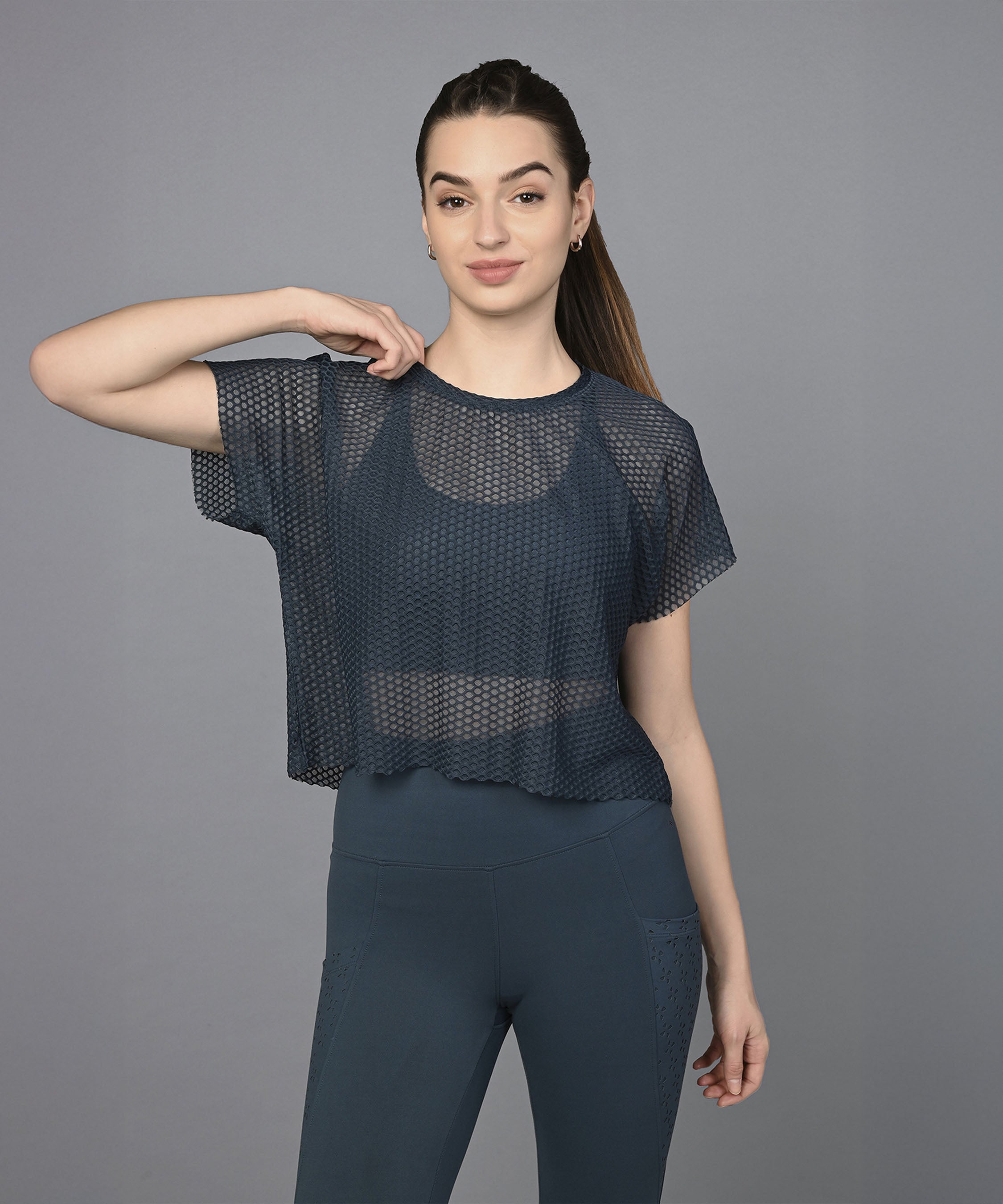 Woman in a Teal Netted Top and matching leggings poses in front of a plain gray background.