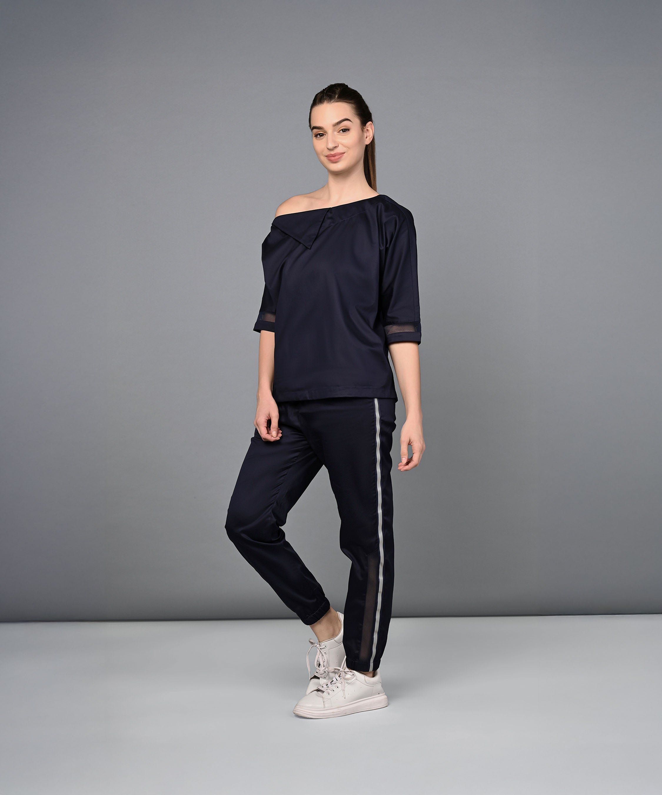 A woman wears the Off Shoulder Nebula Navy Co-ord Set, made from 100% cotton with matching side-striped pants, posed against a gray background.