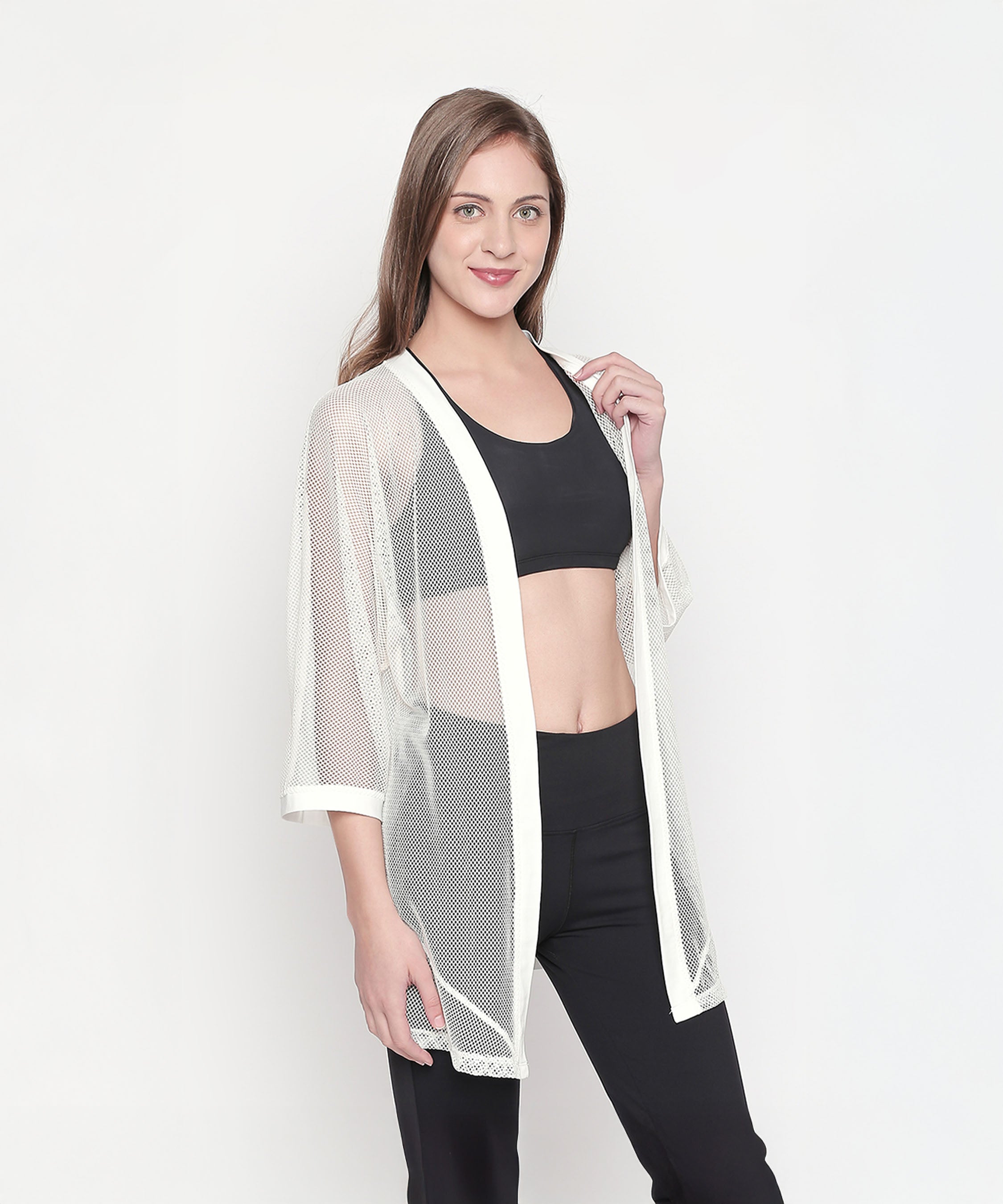 Woman in black sportswear and a sheer Loose Fit 3/4th Sleeve White Shrug for Women poses against a plain white background, highlighting an effortless athleisure look.