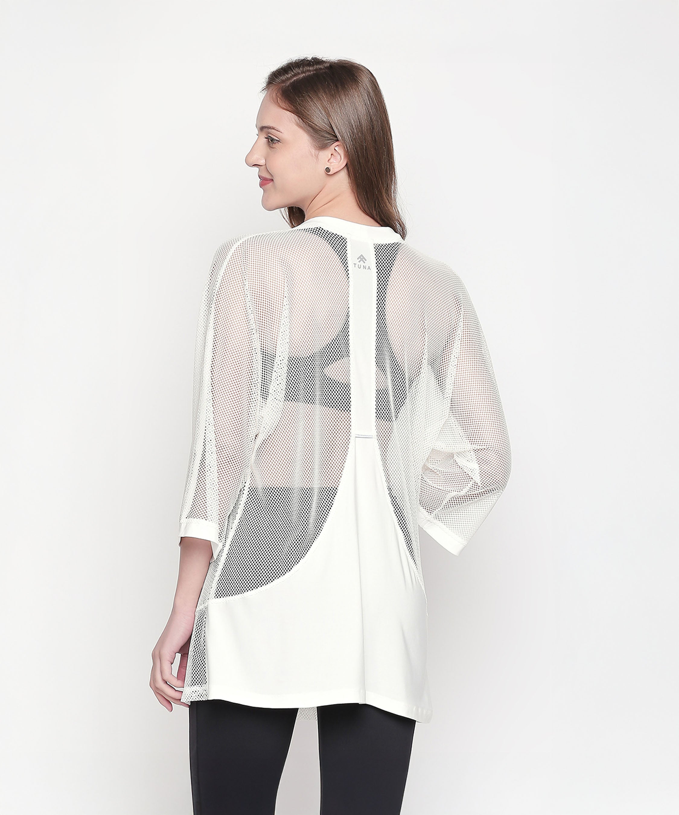 Woman in a Loose Fit 3/4th Sleeve White Shrug and black leggings stands with her back to the camera against a white background, highlighting a stylish athleisure ensemble.