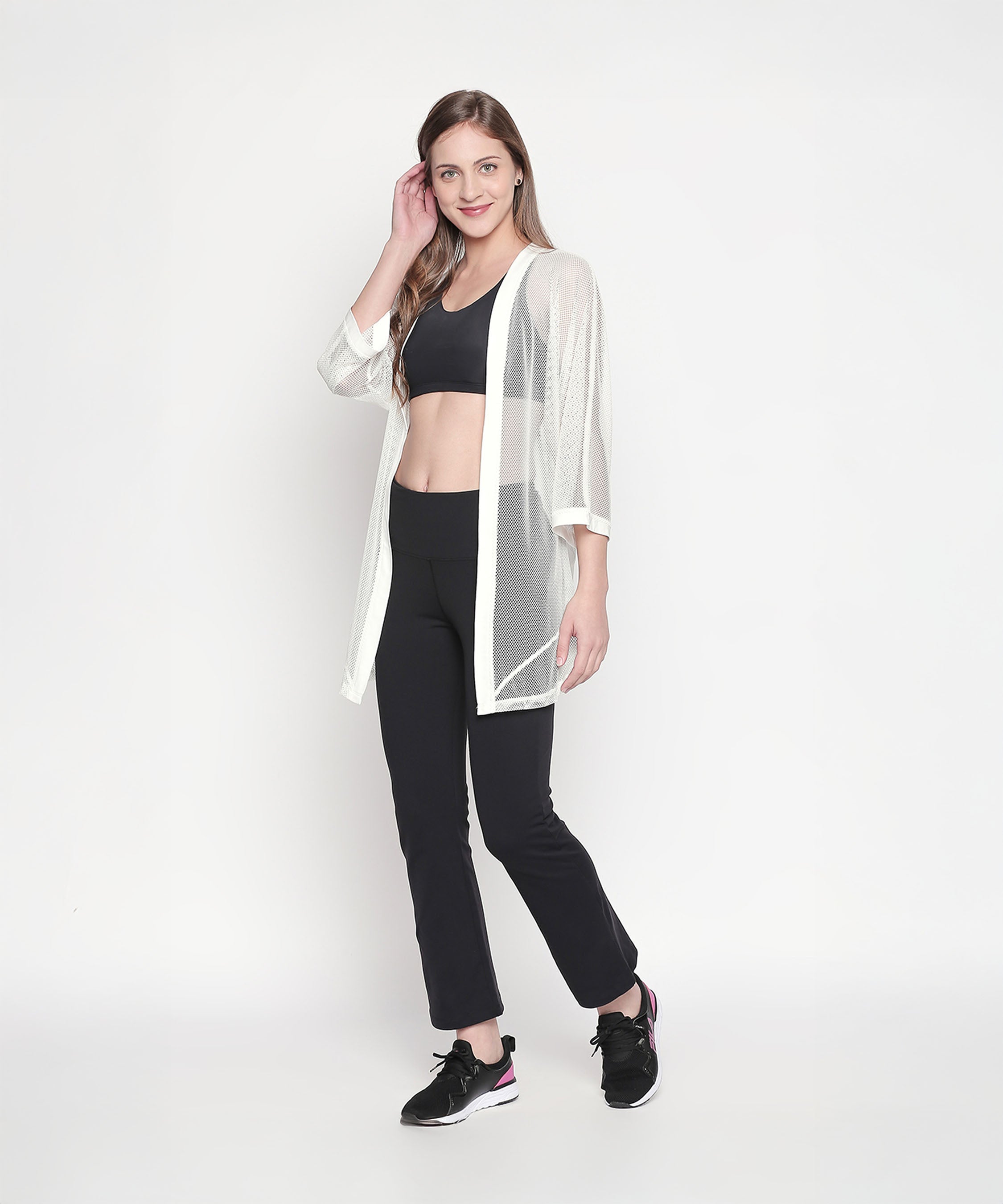 A woman models a Loose Fit 3/4th Sleeve White Shrug for Women over black sportswear against a plain white background for a chic, effortless athleisure look.