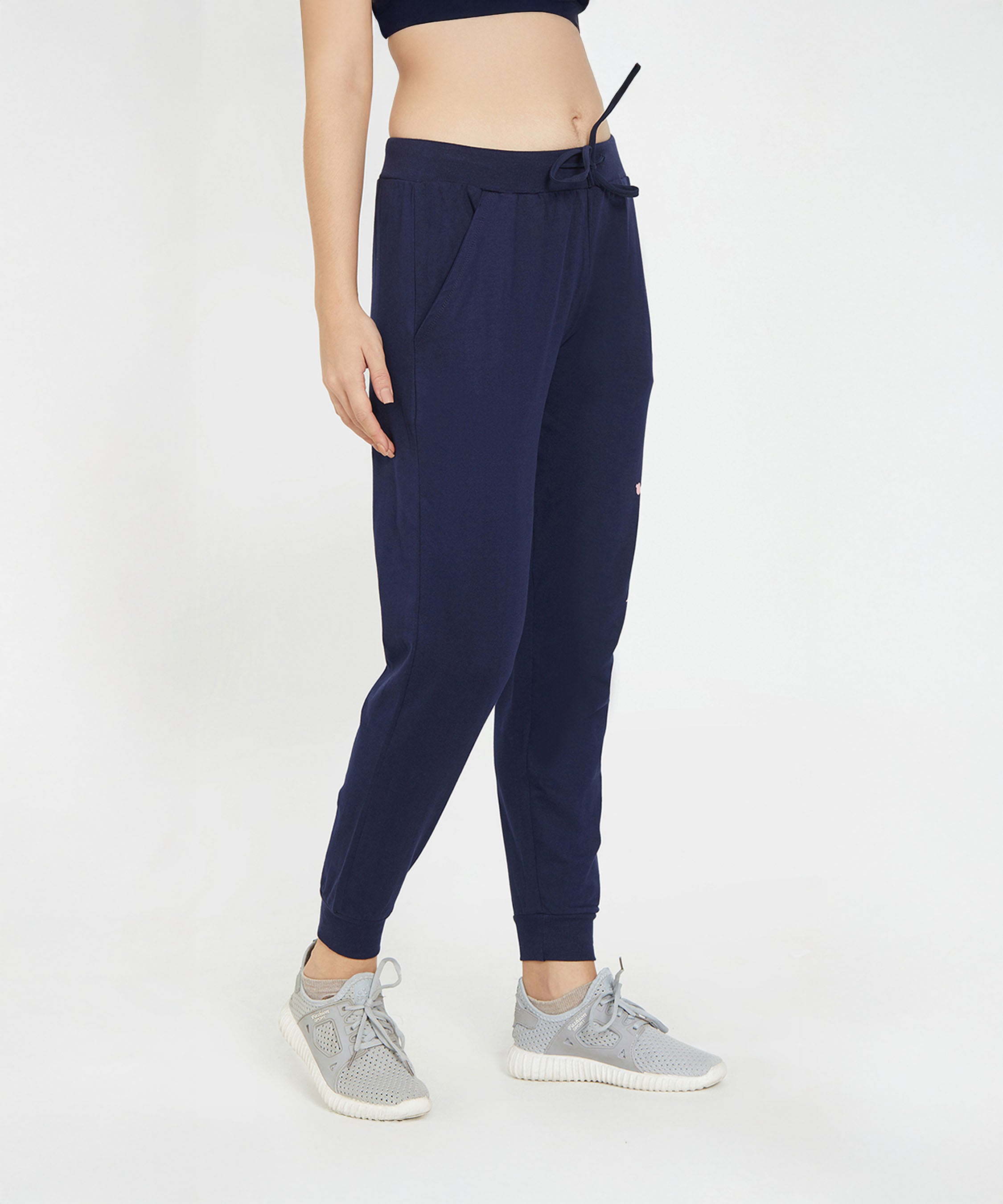 A person wearing Ashtanga Series Blue Joggers, gray sneakers, and a dark crop top stands against a white background.