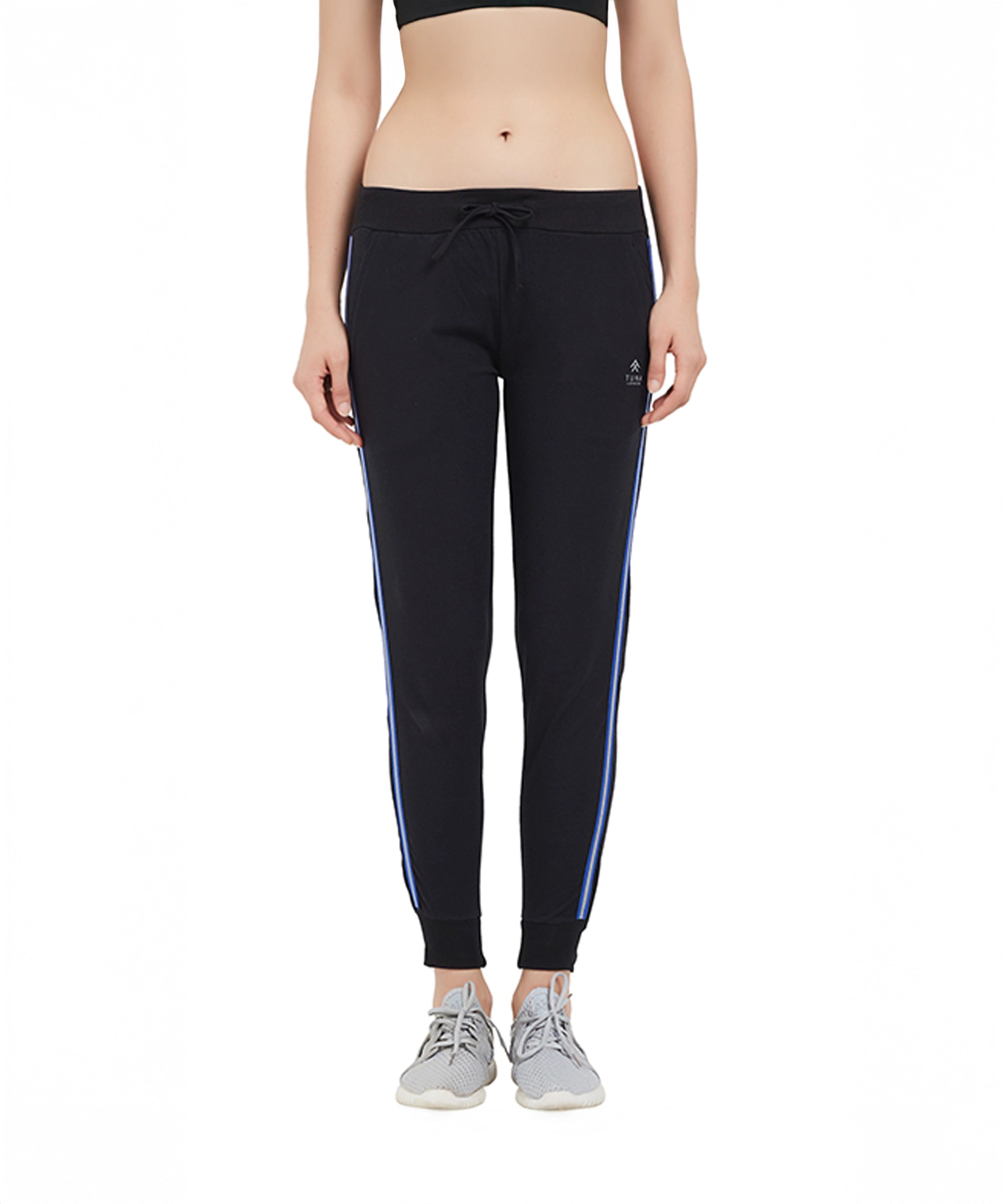 Woman wearing Classic Joggers TLC02SS featuring a sporty side stripe and tapered fit, paired with a black sports bra and gray sneakers, standing on a white background.