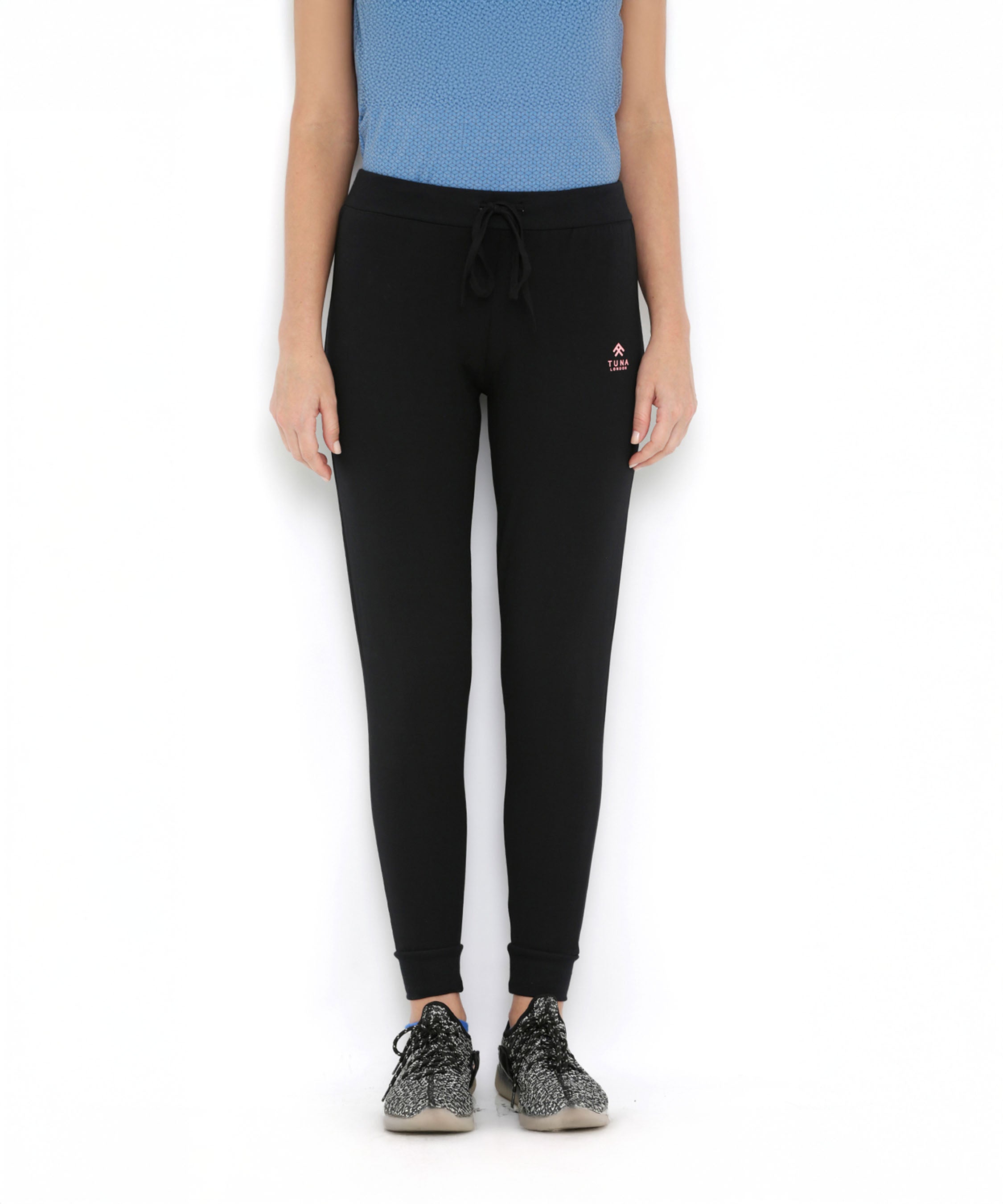 A woman in Black Classic Joggers TLC02 with a slim tapered fit, paired with a blue top and sneakers, stands against a plain white background.