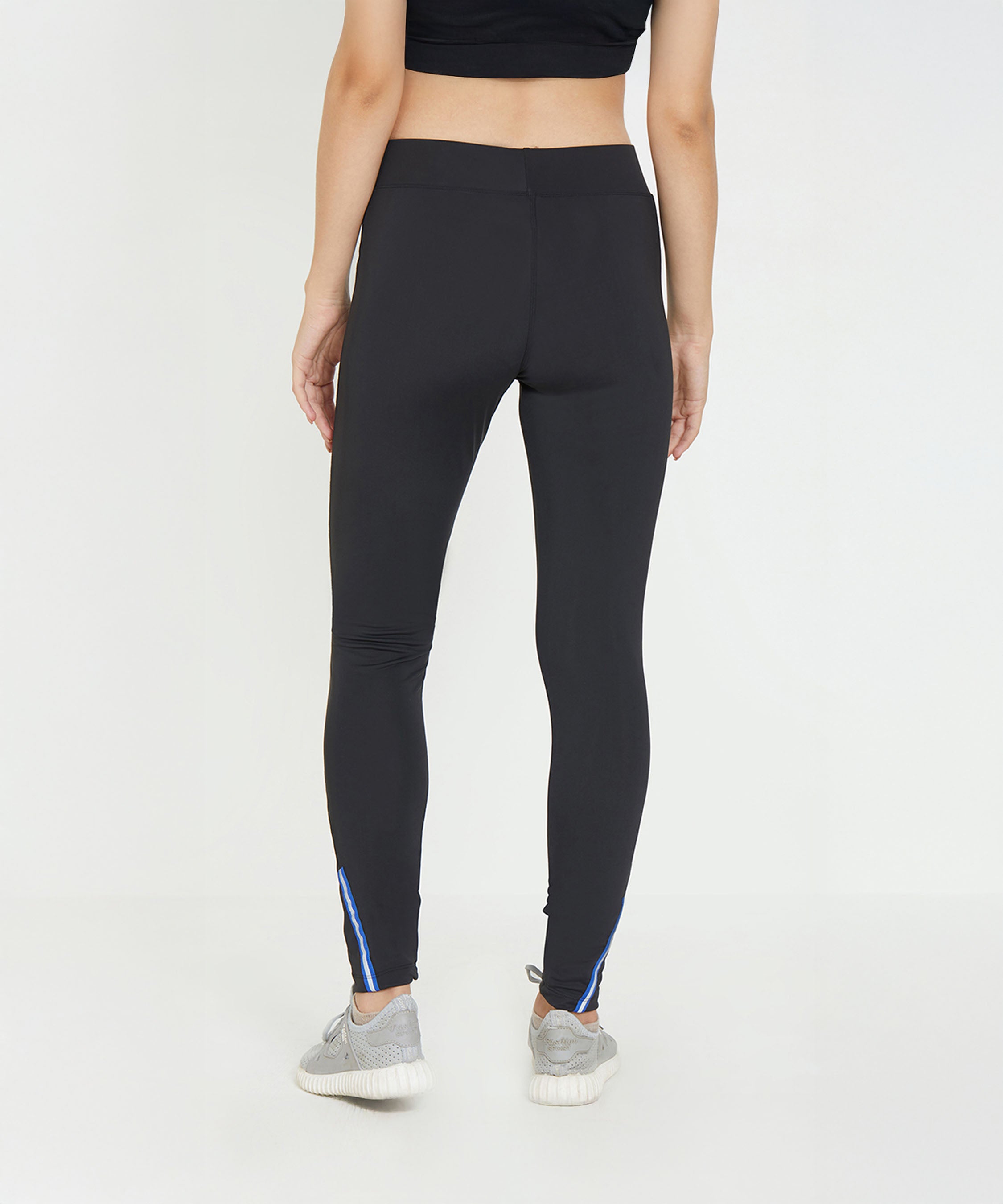 Woman wearing Black Poly Blend Tights for Women - LG10 with a high-rise waistband and sneakers, viewed from the back against a plain white background—ideal workout essentials for any fitness routine.
