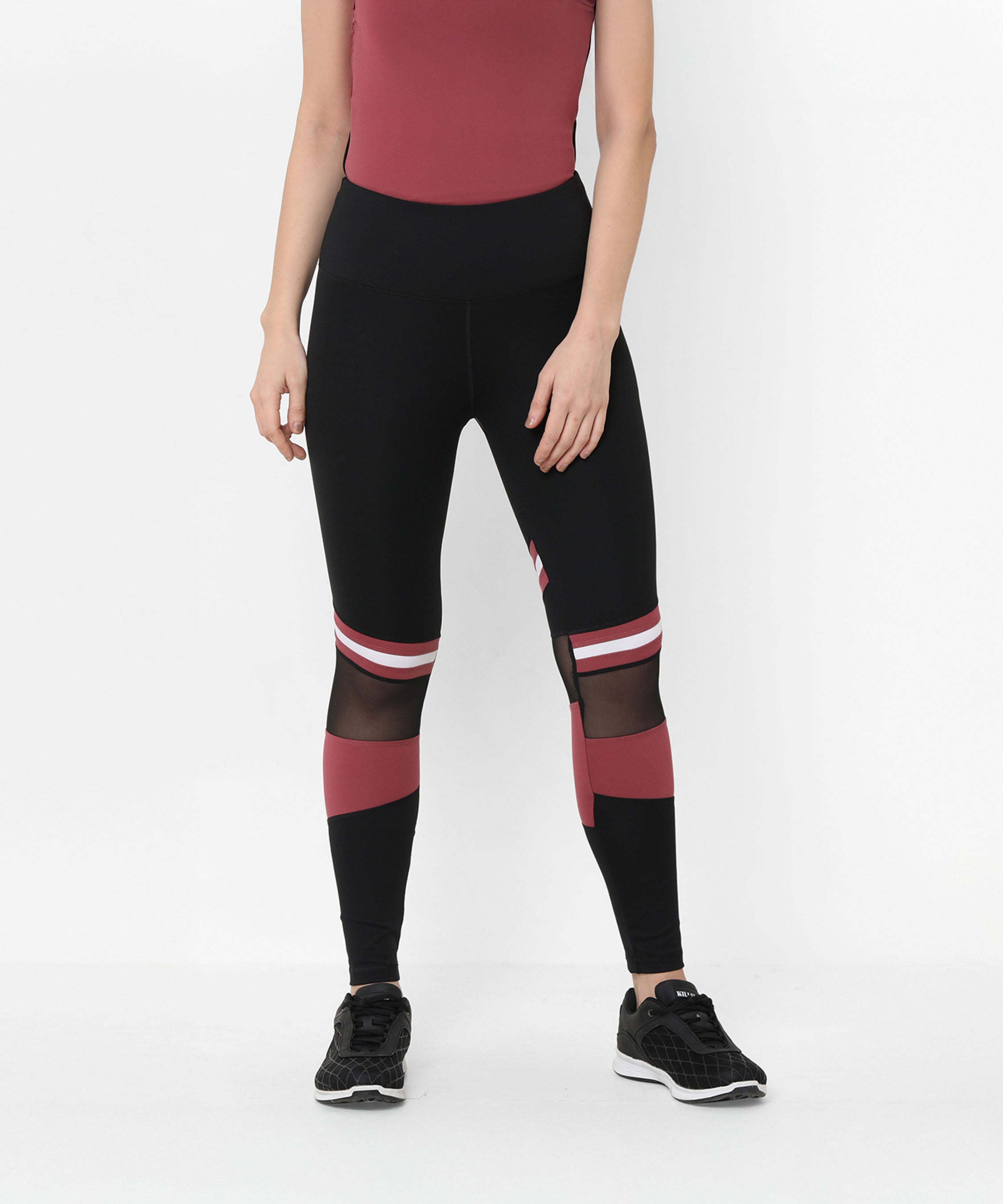Woman wearing Sienna Black High Waisted Leggings with mesh panels, a maroon top, and black sneakers, standing.