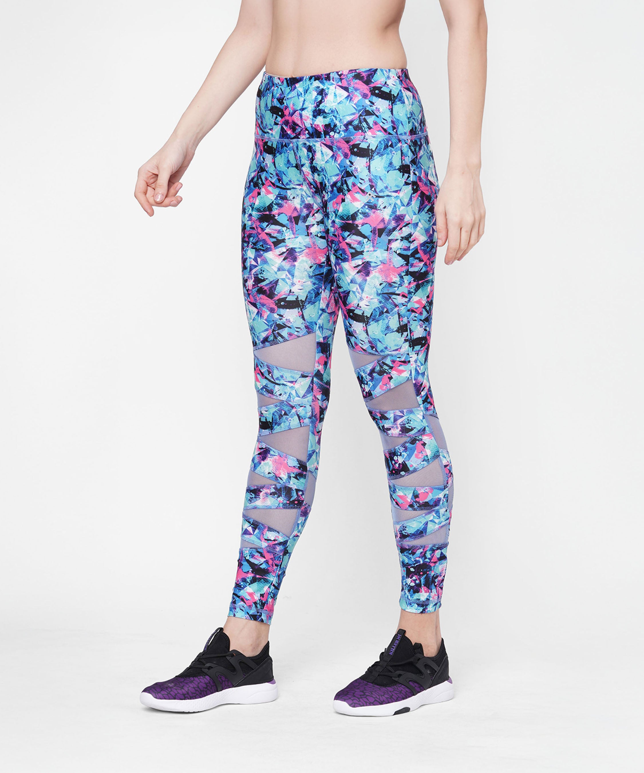 A woman models the Amira Printed Leggings with vibrant florals and mesh panels, matched with black-purple sneakers, standing against a white background.