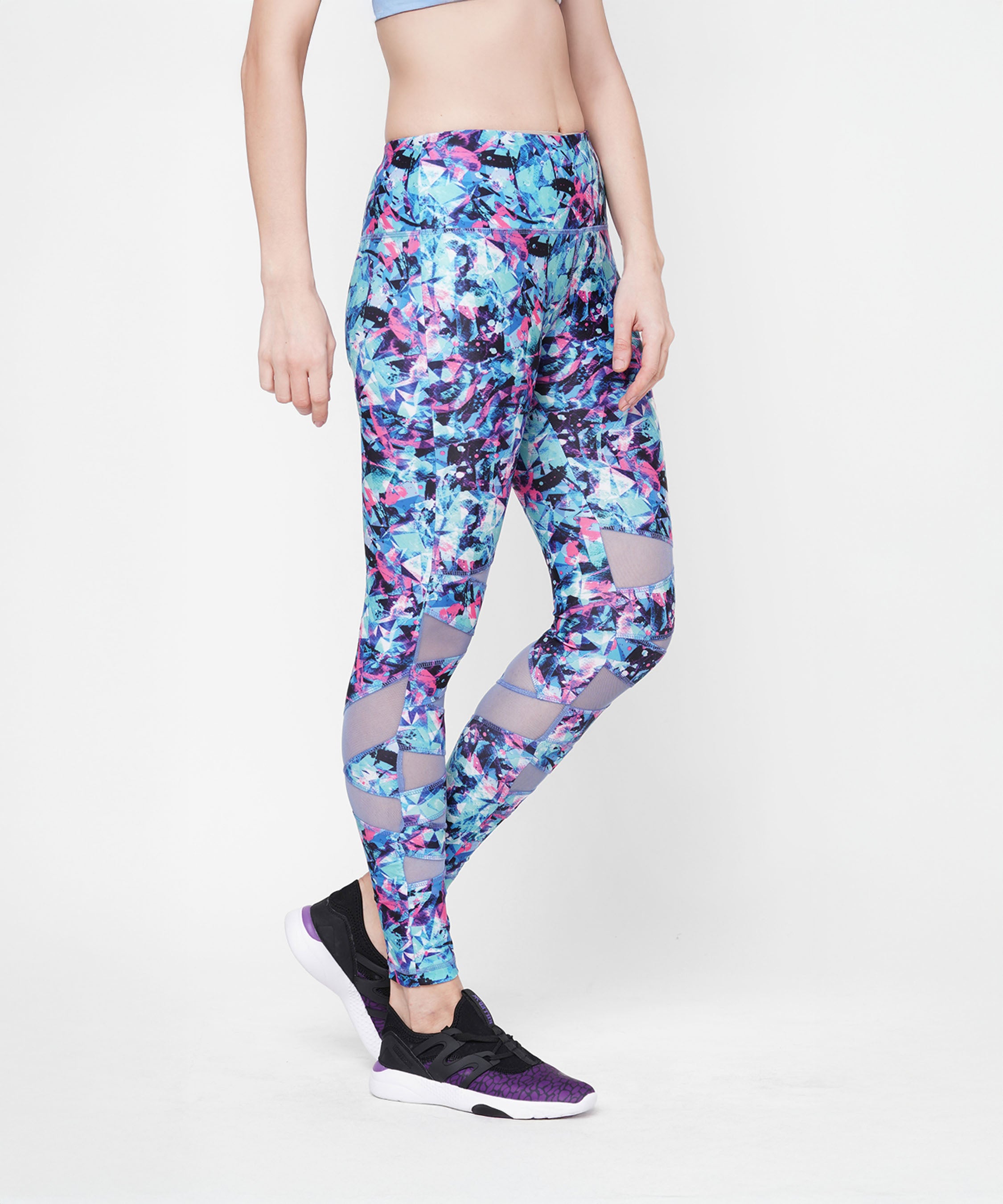 Woman wearing colorful blue and purple Amira Printed Leggings, black sneakers, and a light blue sports bra.