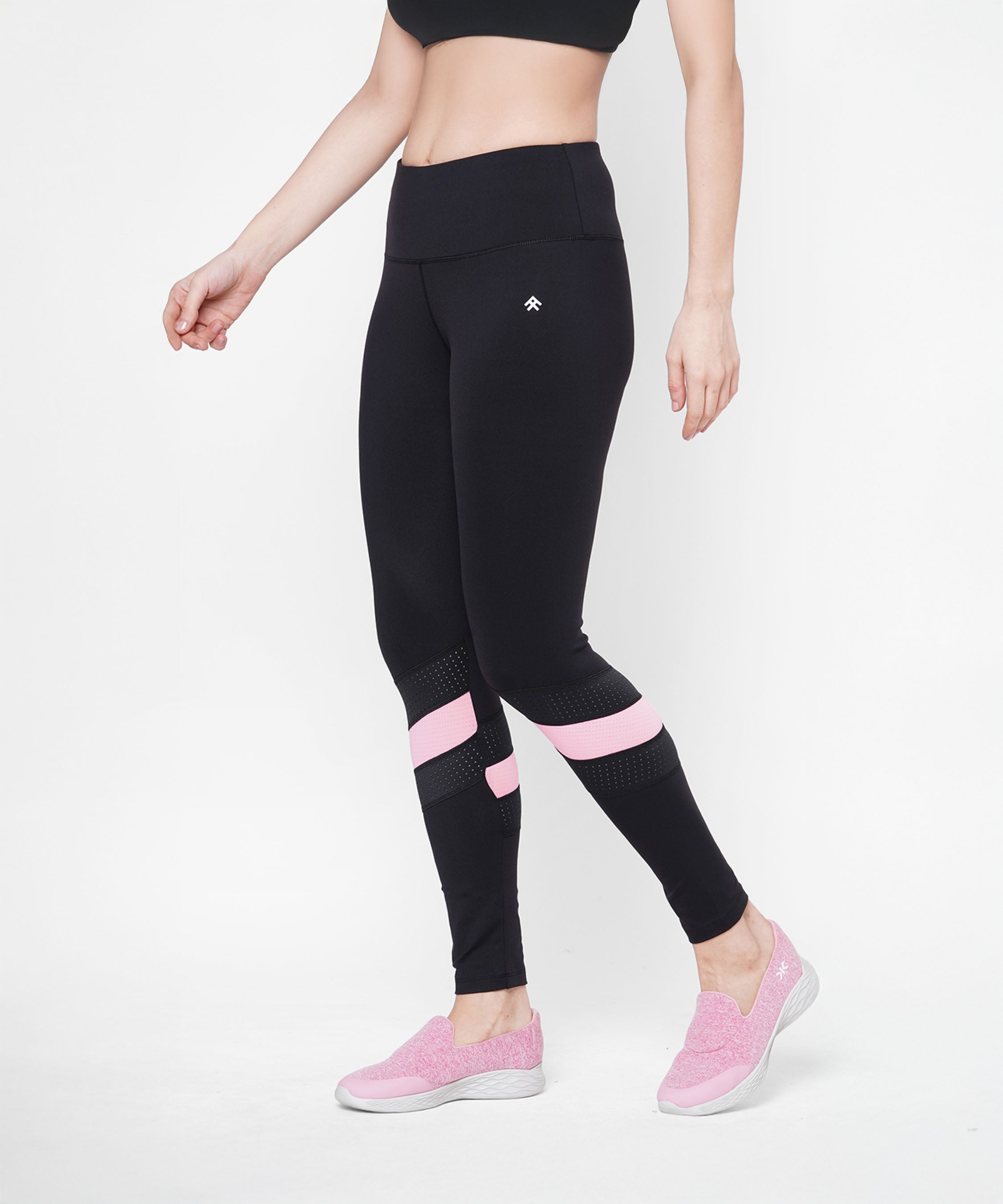 A woman is wearing the Black High Waisted Compression Legging With a Neon Pink Patch, paired with a black sports bra and pink slip-on shoes. Made from four-way stretch compression fabric for comfort and support.