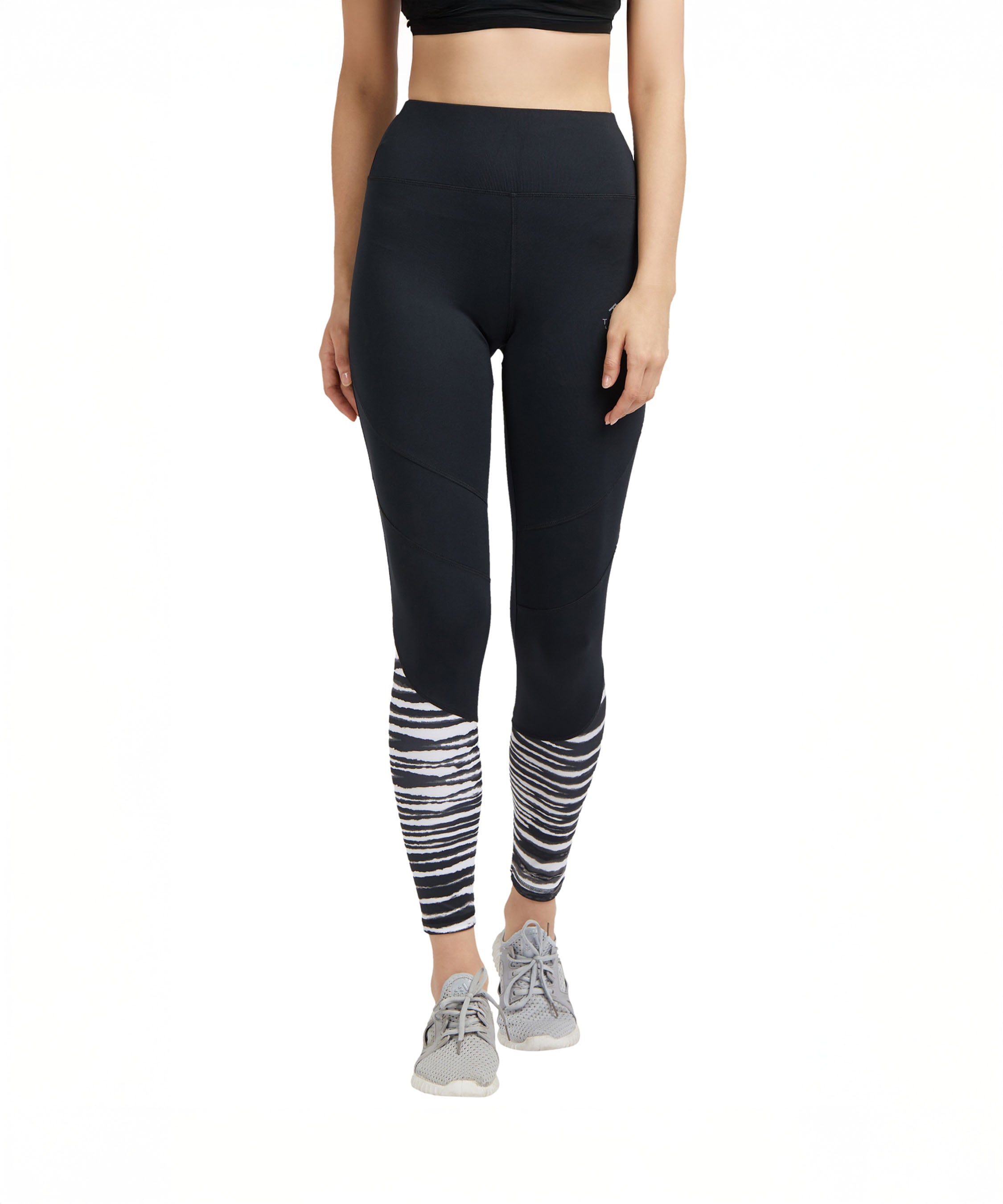 A woman wears Black High Waisted Compression Sports Leggings With Zebra Print, paired with grey sneakers and a black crop top.