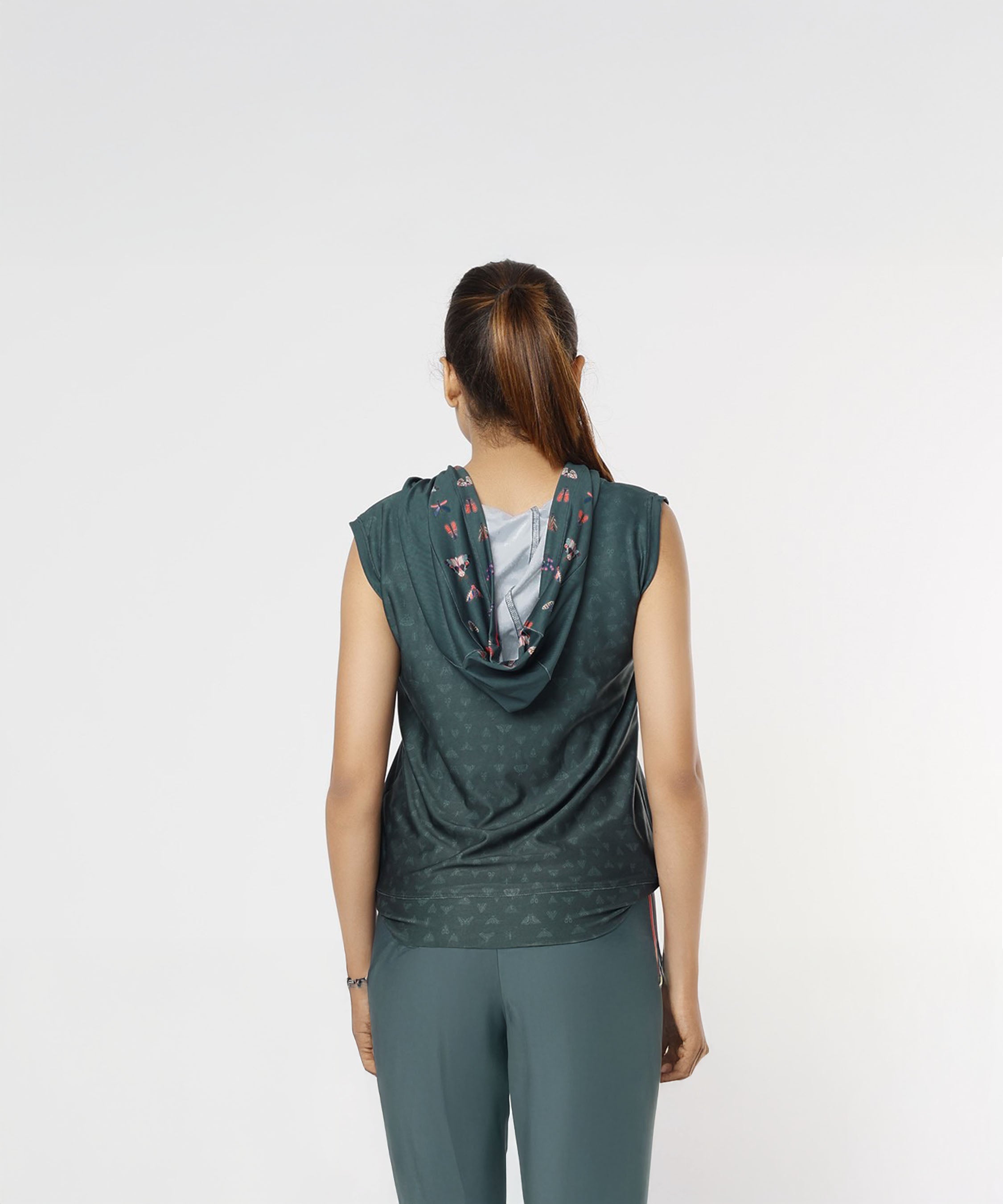 A woman with a ponytail stands facing away, wearing the Tuna Active Teal Hooded Top and matching ombre teal workout pants.