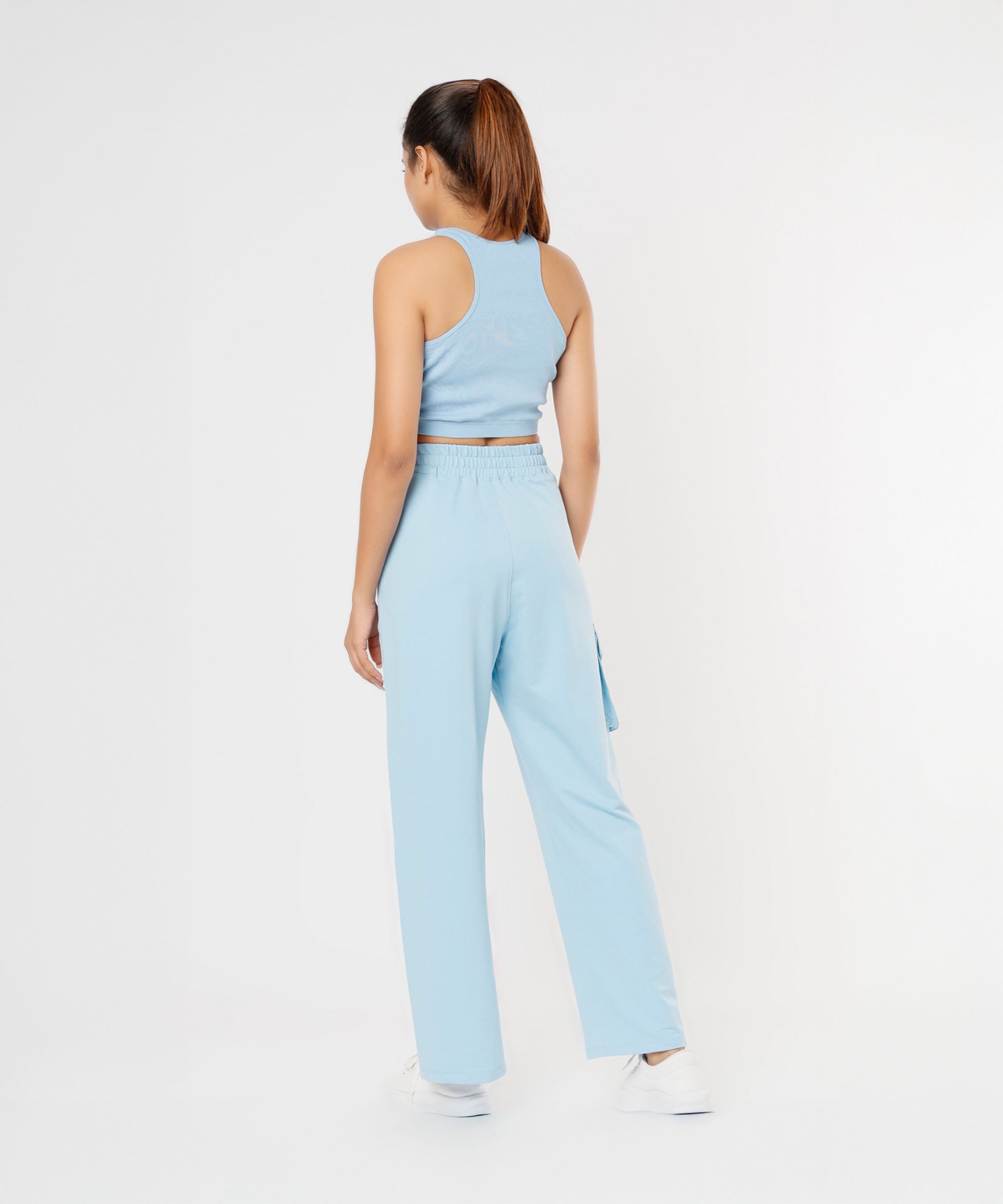 A woman stands with her back to the camera, modeling the Blue Dream Crop Top in powder blue with matching pants.