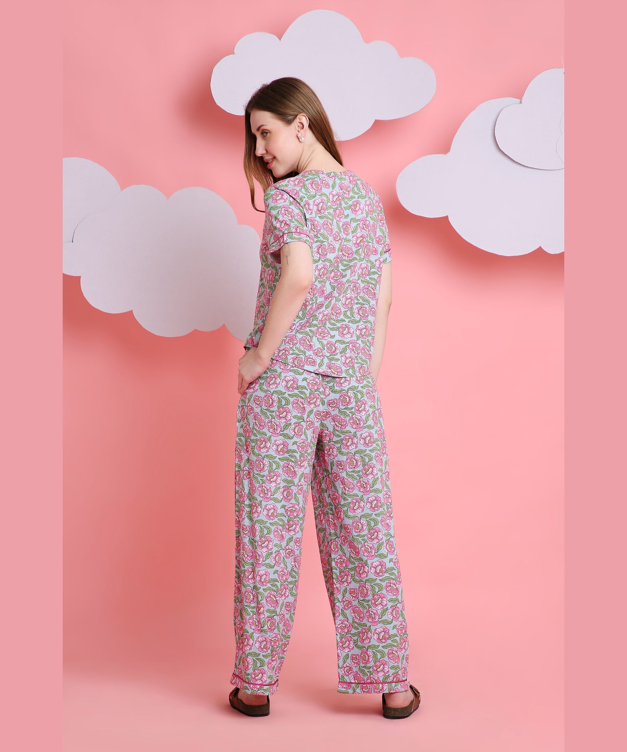 A woman shows off the Floral Love night suit with her back to the camera against a pink backdrop and paper clouds, highlighting its breathable fabric for comfortable sleepwear.