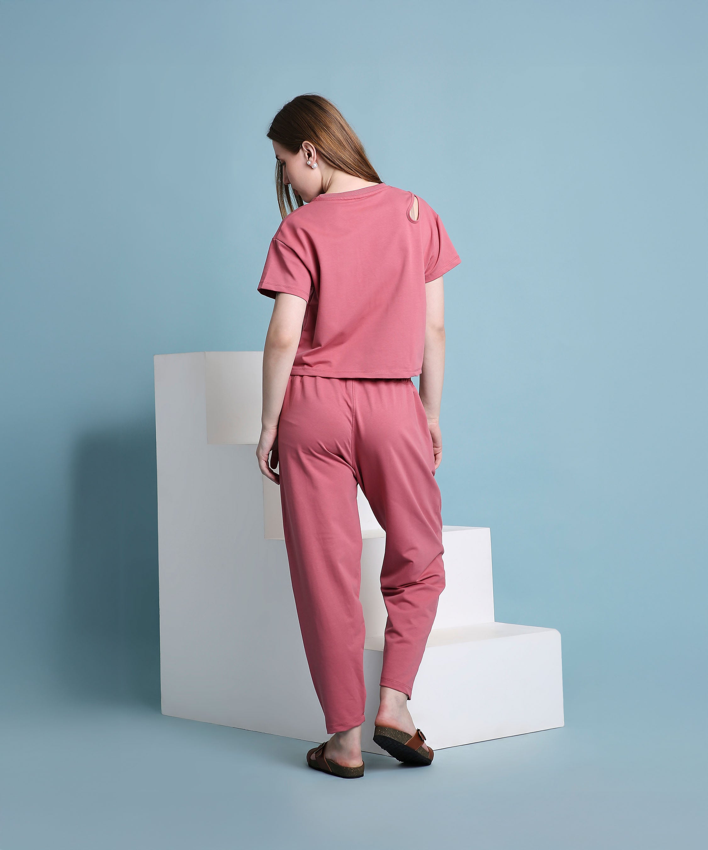 A woman wearing the Vintage Pink Knit Cord Set stands by white steps, facing away, with a light blue background.