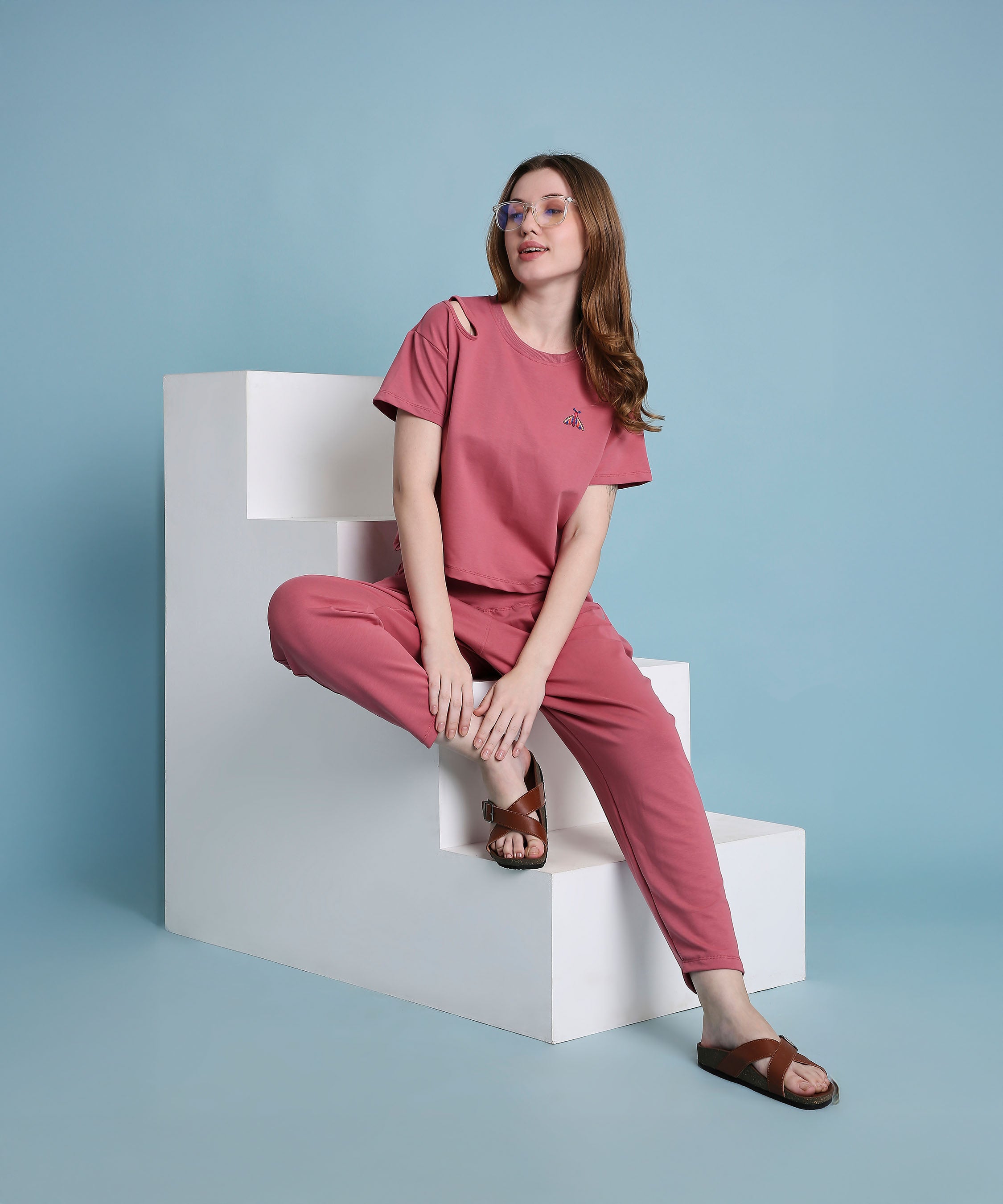 A woman wearing the Vintage Pink Knit Cord Set sits on white geometric steps against a light blue background.