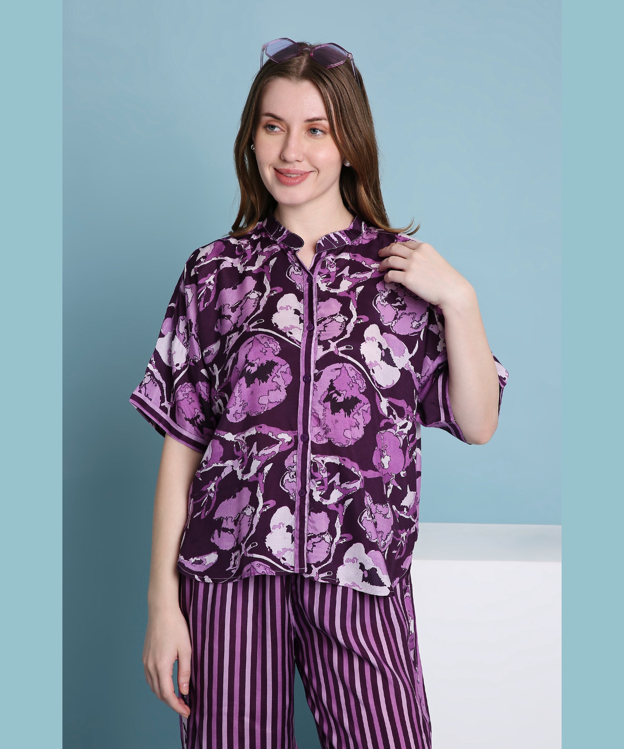 Smiling woman wears the Purple Breeze pyjama set, featuring a comfortable mix of floral and striped patterns, against a blue background.