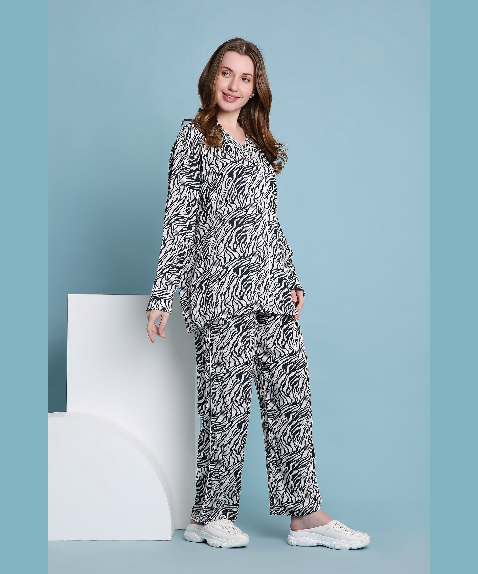 Smiling woman wears the Zeba relaxed fit zebra print pyjama set with white slip-on shoes, posing against a blue background.