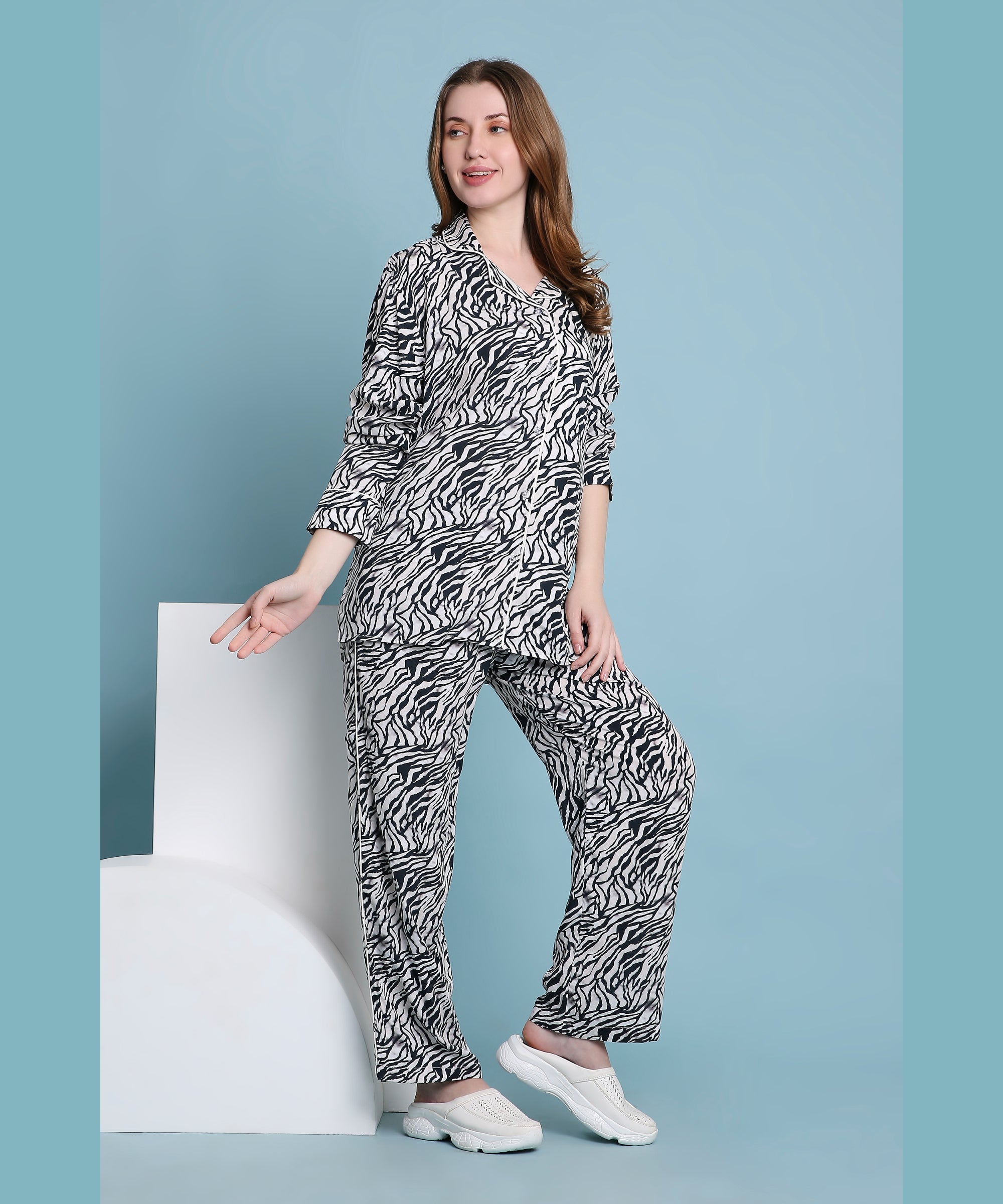 A woman poses against a light blue background wearing the Zeba relaxed fit zebra print pyjama set and white sneakers.