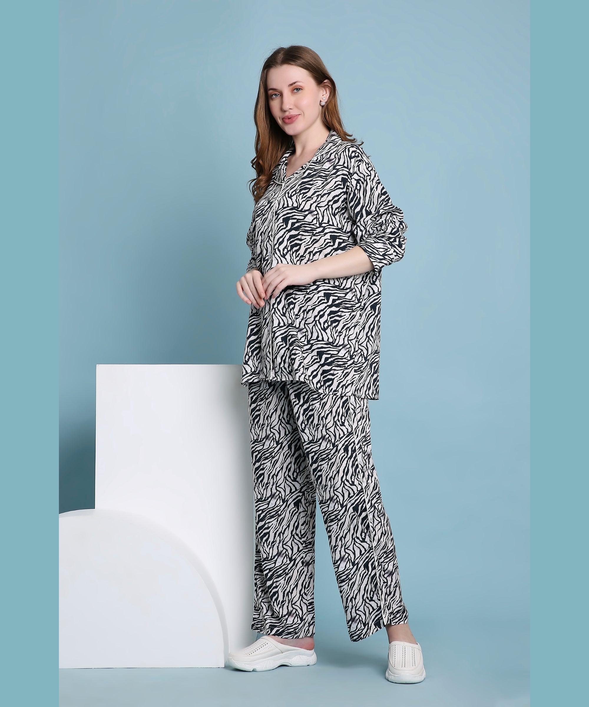 A woman poses confidently against a blue background with white props, wearing the Zeba relaxed fit zebra print pyjama set paired with white sneakers.