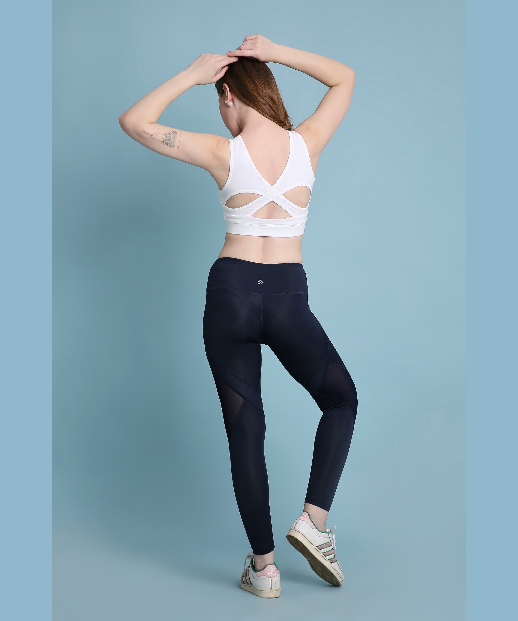 Woman in activewear posing with hands on head, wearing a white sports bra and Indigo poly blended leggings.