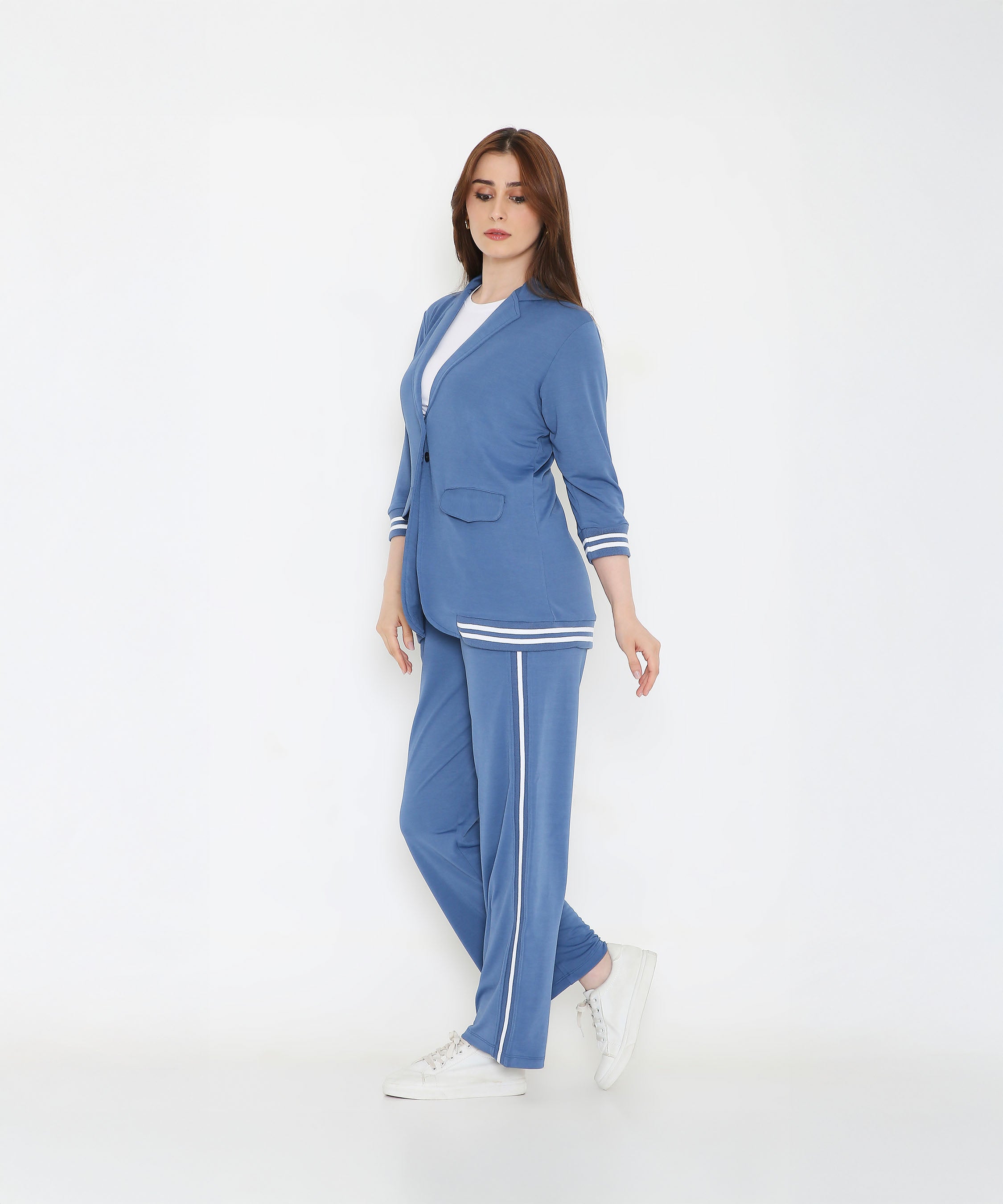 A woman stands confidently in the Atlantic Blue Athleisure Blazer Jacket and Track Set with white stripes and white sneakers against a plain white background.